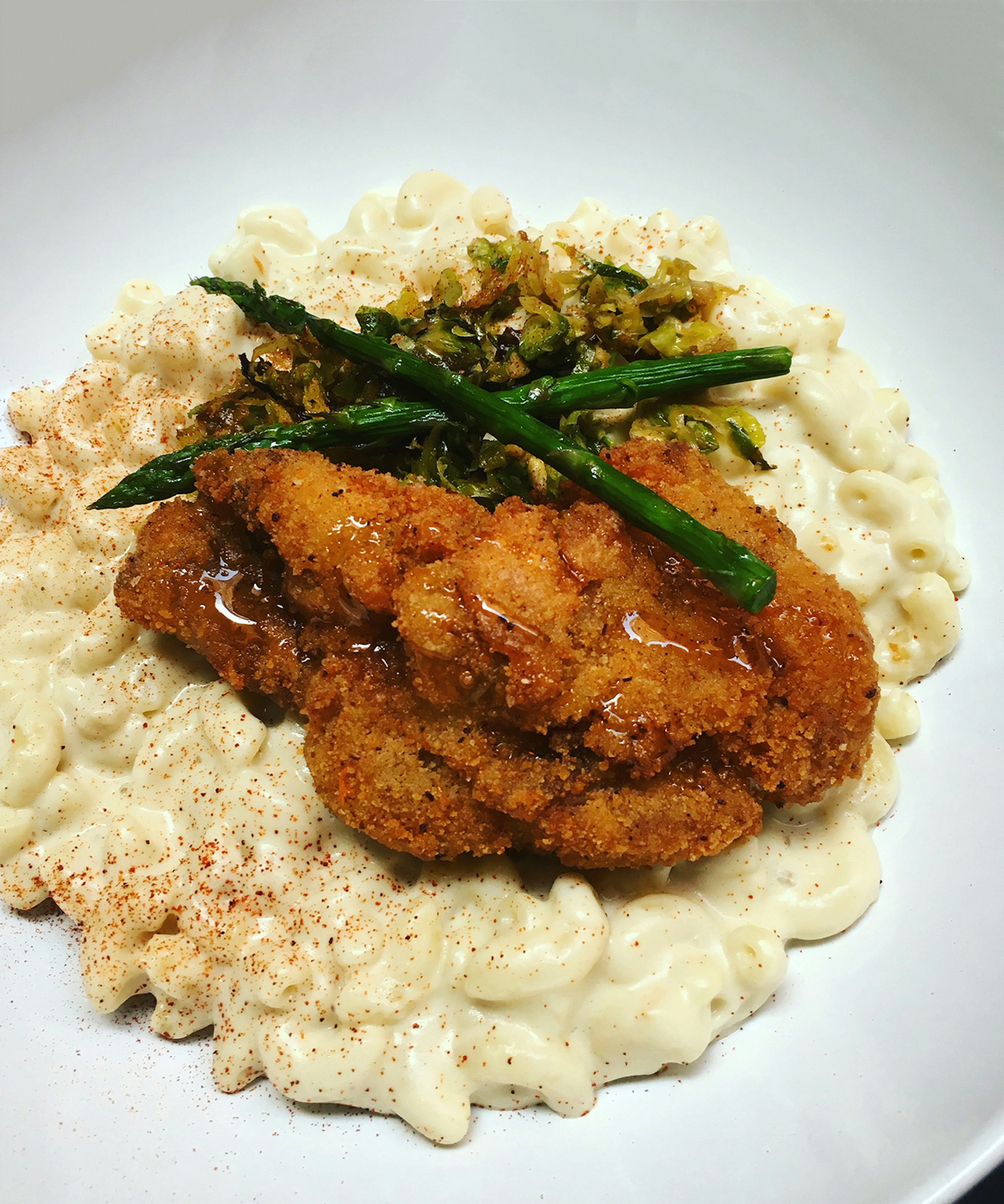 close-up shot of pale yellow mac-and-cheese sprinkled with paprika and topped with fried seitan, on a white plate