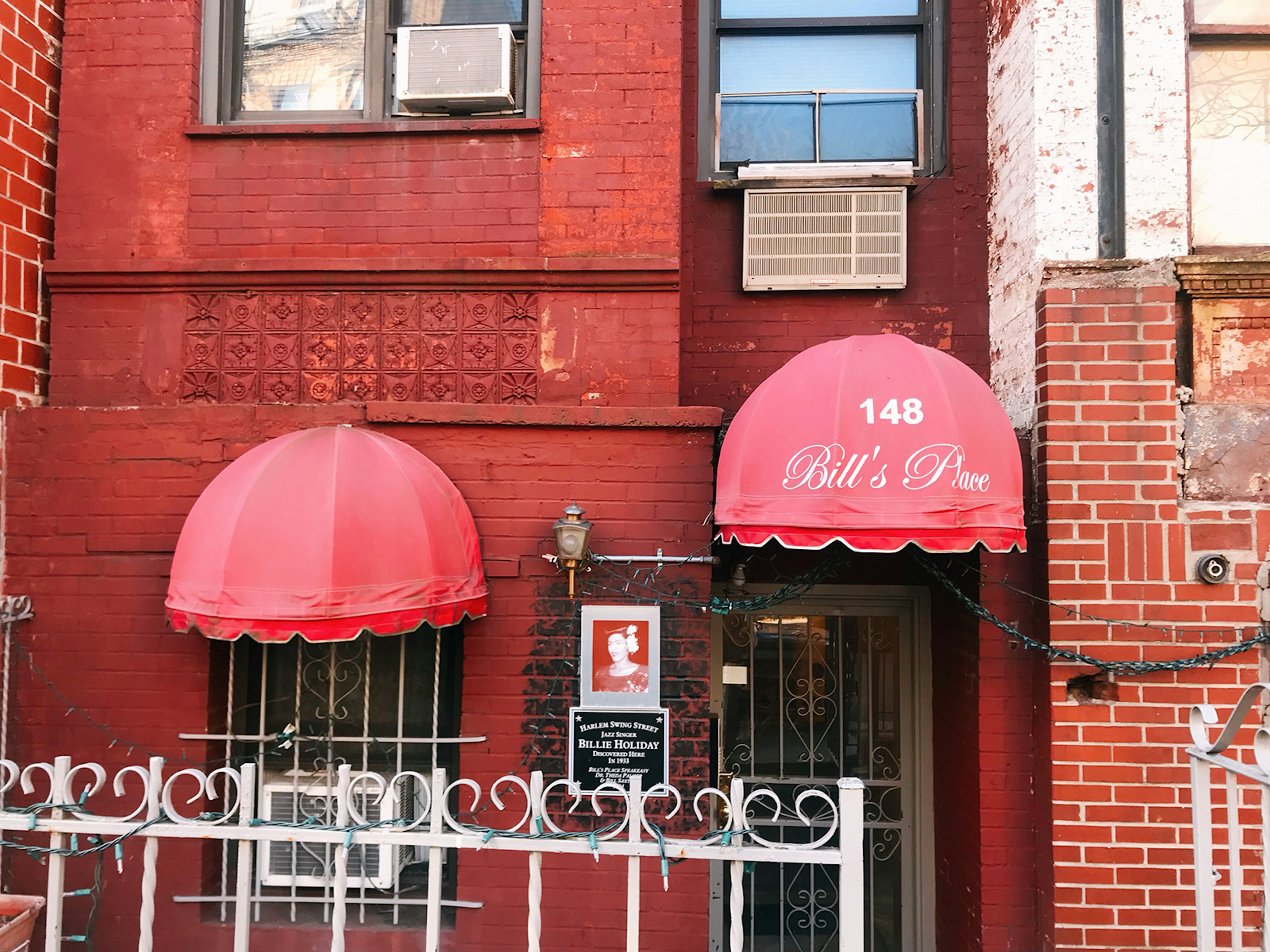 Red brick exterior of a Harlem row house, with red awnings over the door and window reading