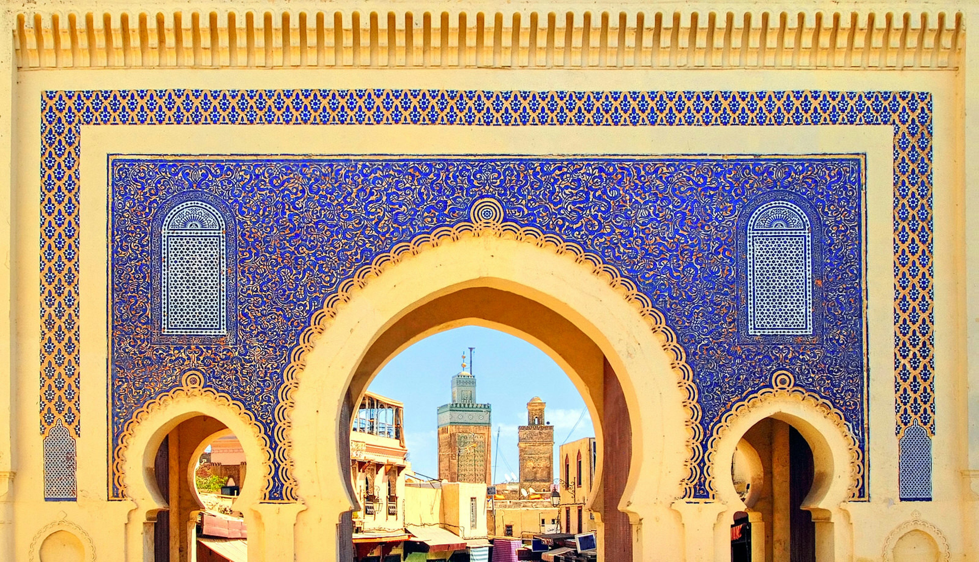 The golden arches of Fez's Blue Gate Bab Boujelud reveal life inside the medina; between the arches and gold trim, the large gate is decorated in delicate blue floral tiles.