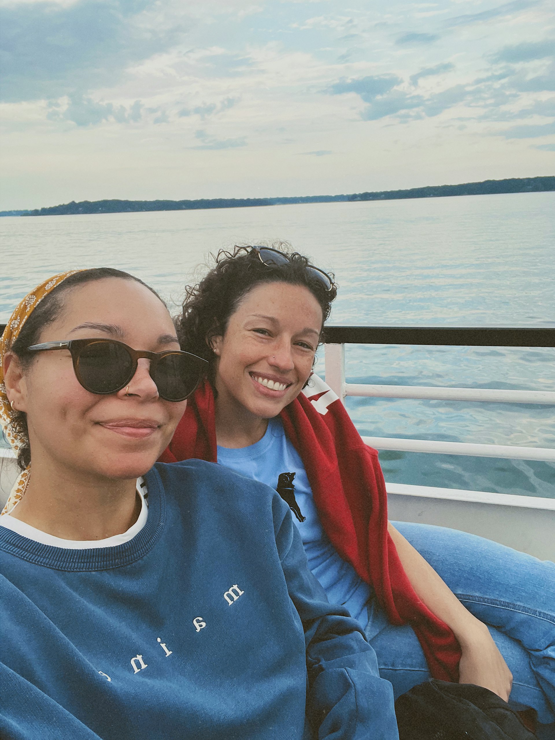 Two women on the top deck of a boat huddle together and pose for a photo