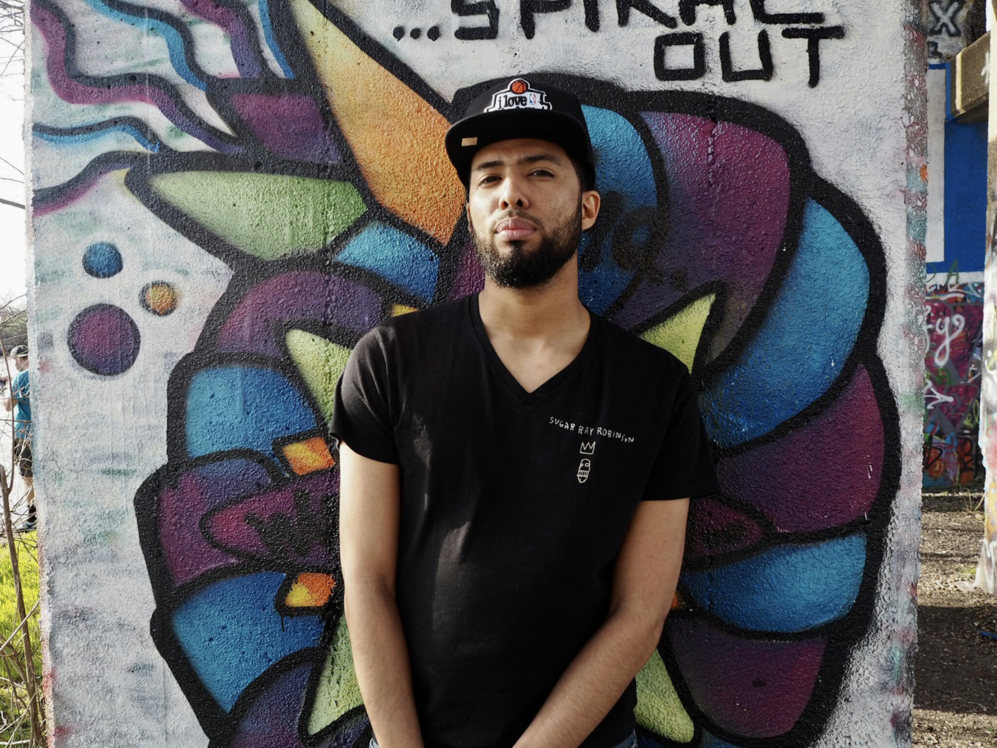 Young man in hat stands in front of blue and purple graffiti at Graffiti Pier in Philadelphia