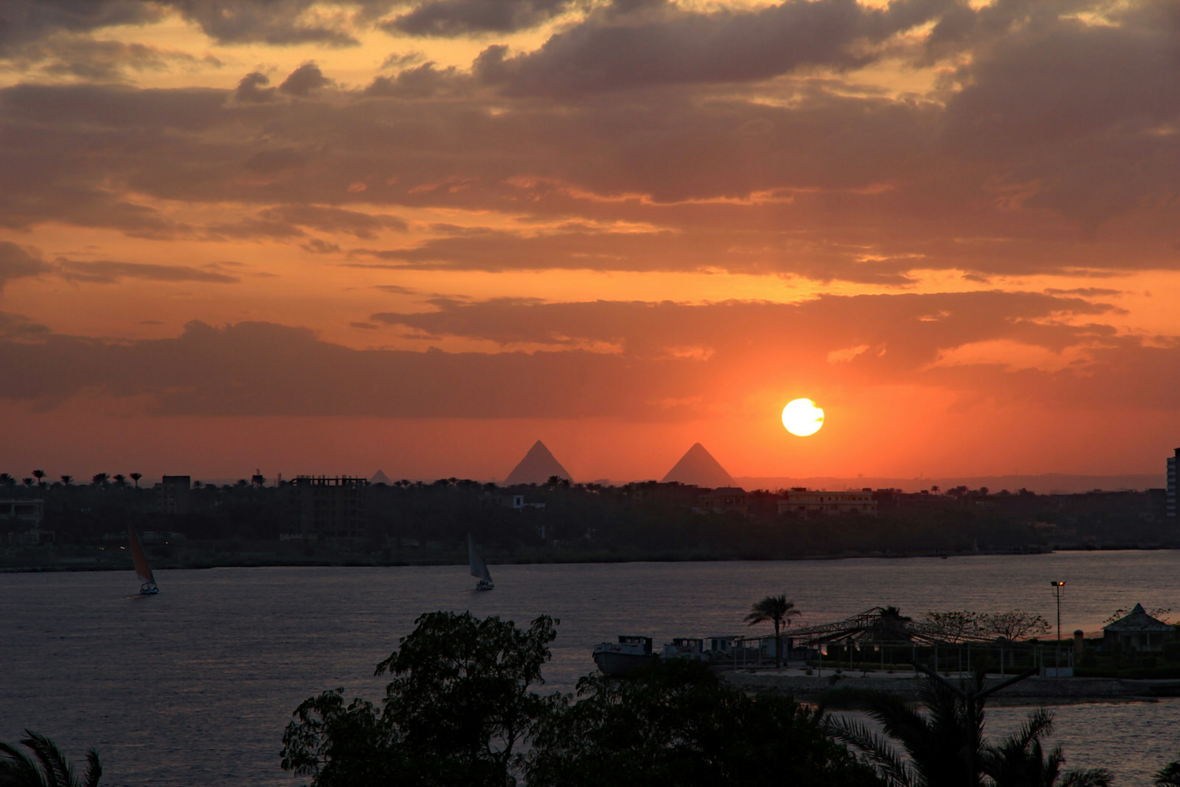 Dramatic fiery red and orange sunset over the River Nile with feluccas calmly sailing and the magnificent Giza pyramids in the background. View from Maadi, Cairo, Egypt. Image by Harry Green / Shutterstock