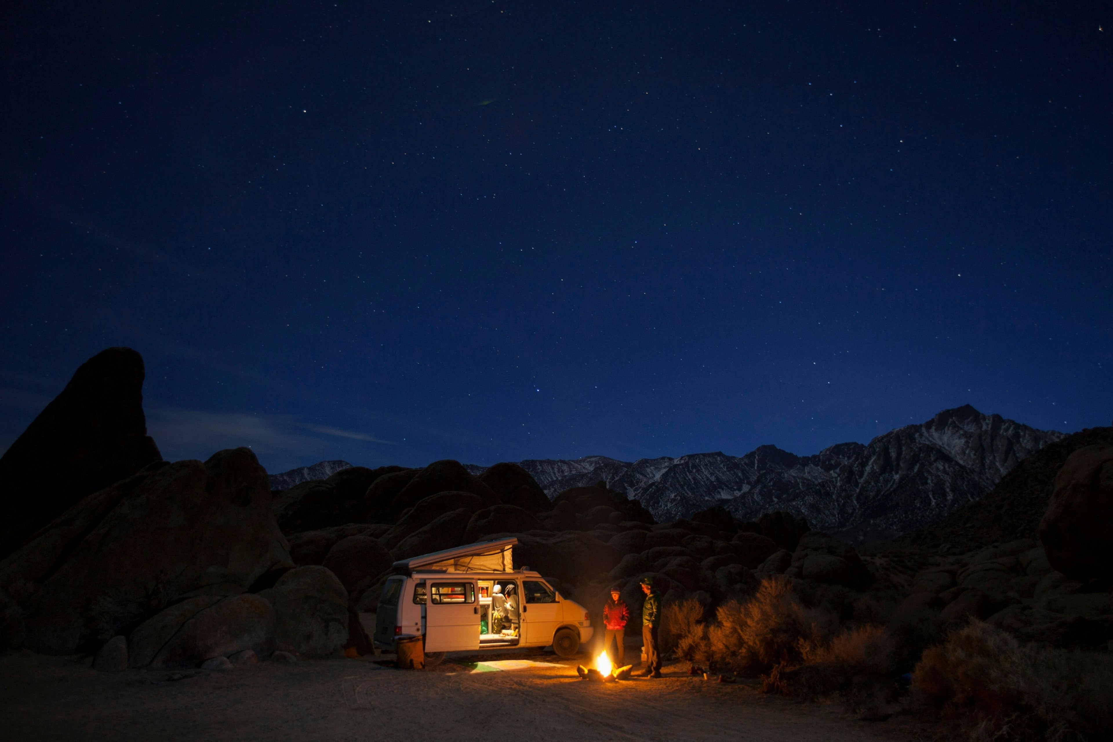 Two people stand by a campfire in front of their motorhome on a camping trip.