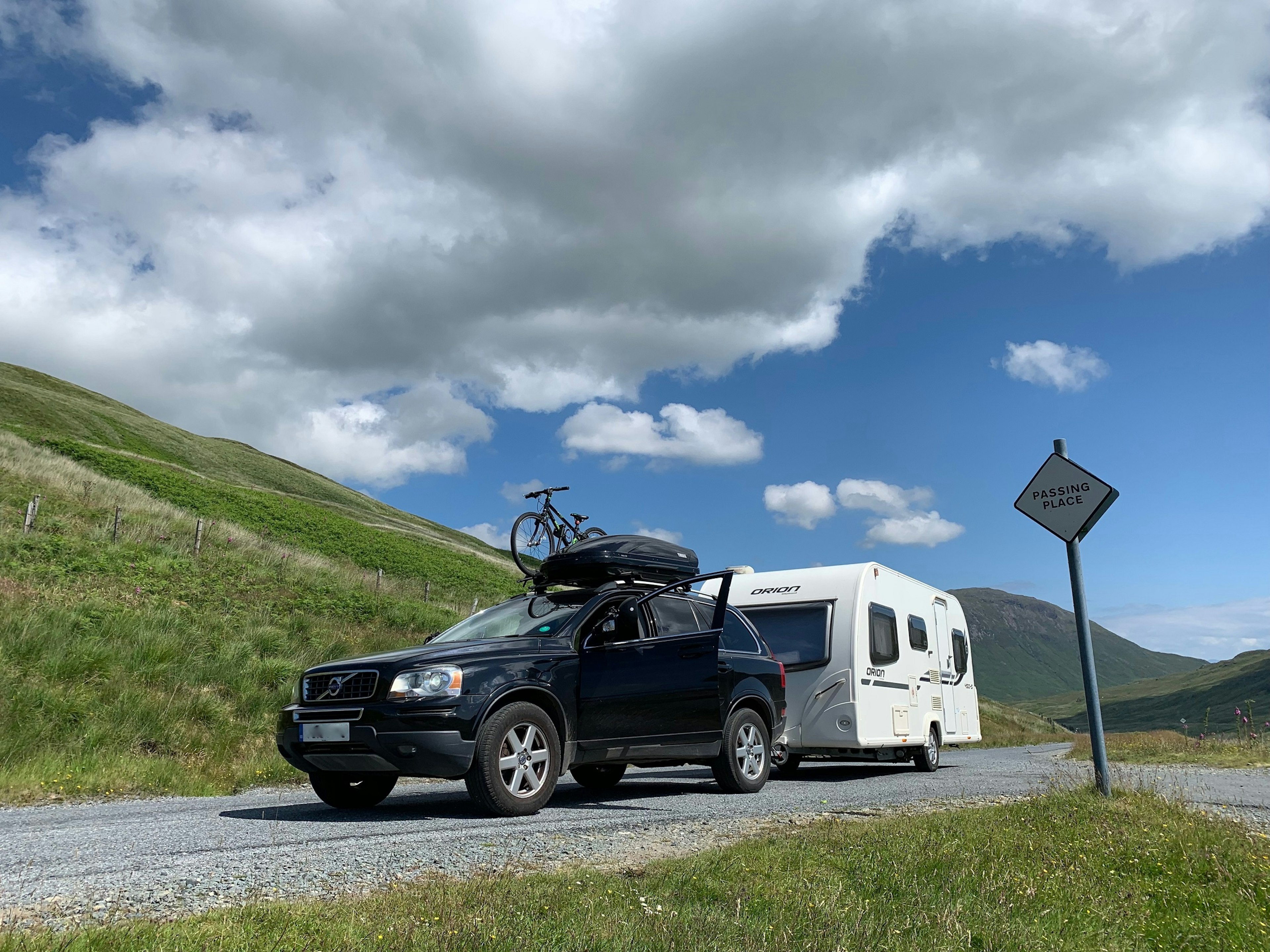 A large black car, with roof box and bike rack, hooked up to a white caravan.