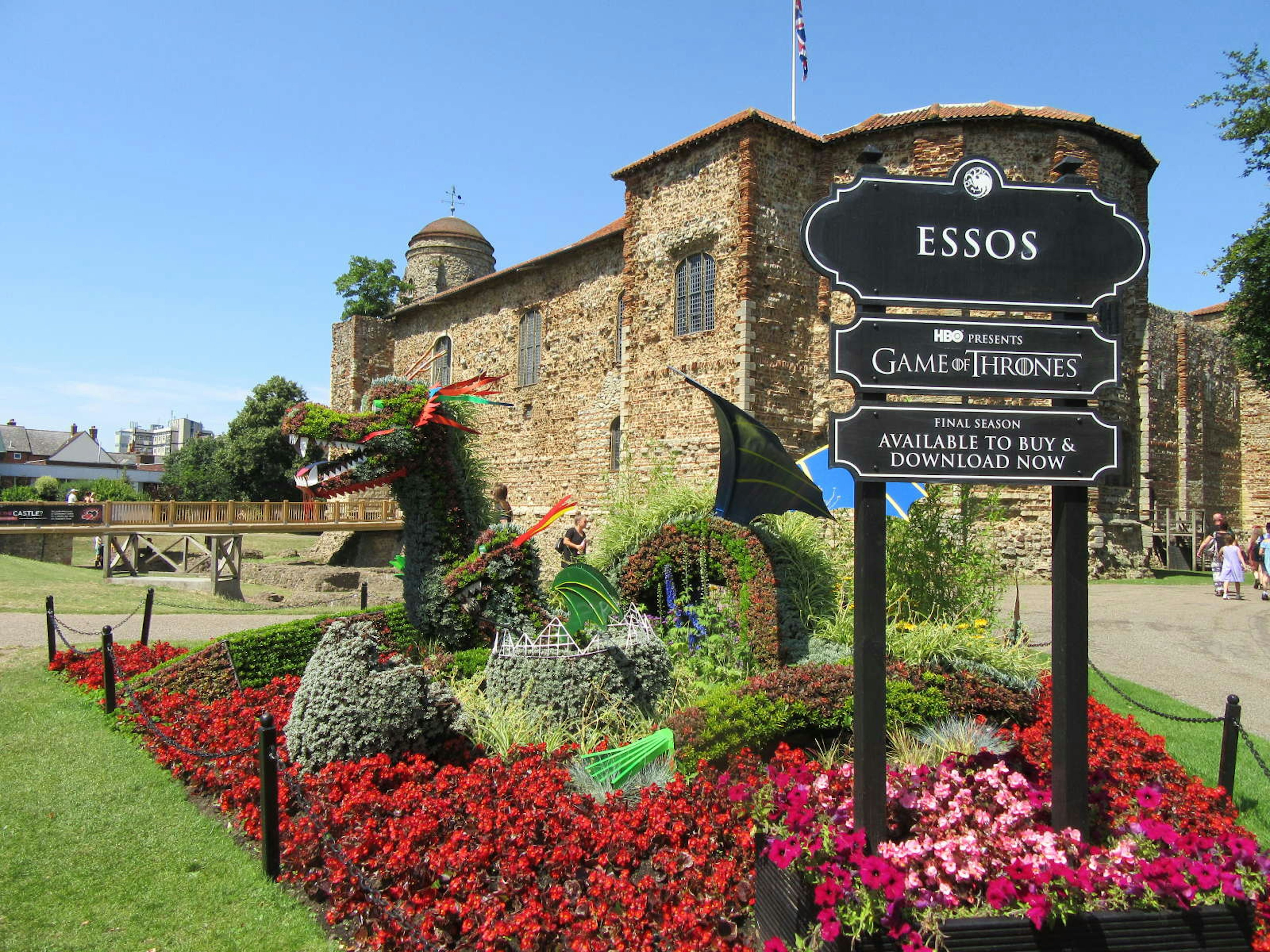 A topiary dragon with a sign advertising HBO's Game of Thrones with Colchester Castle in the background