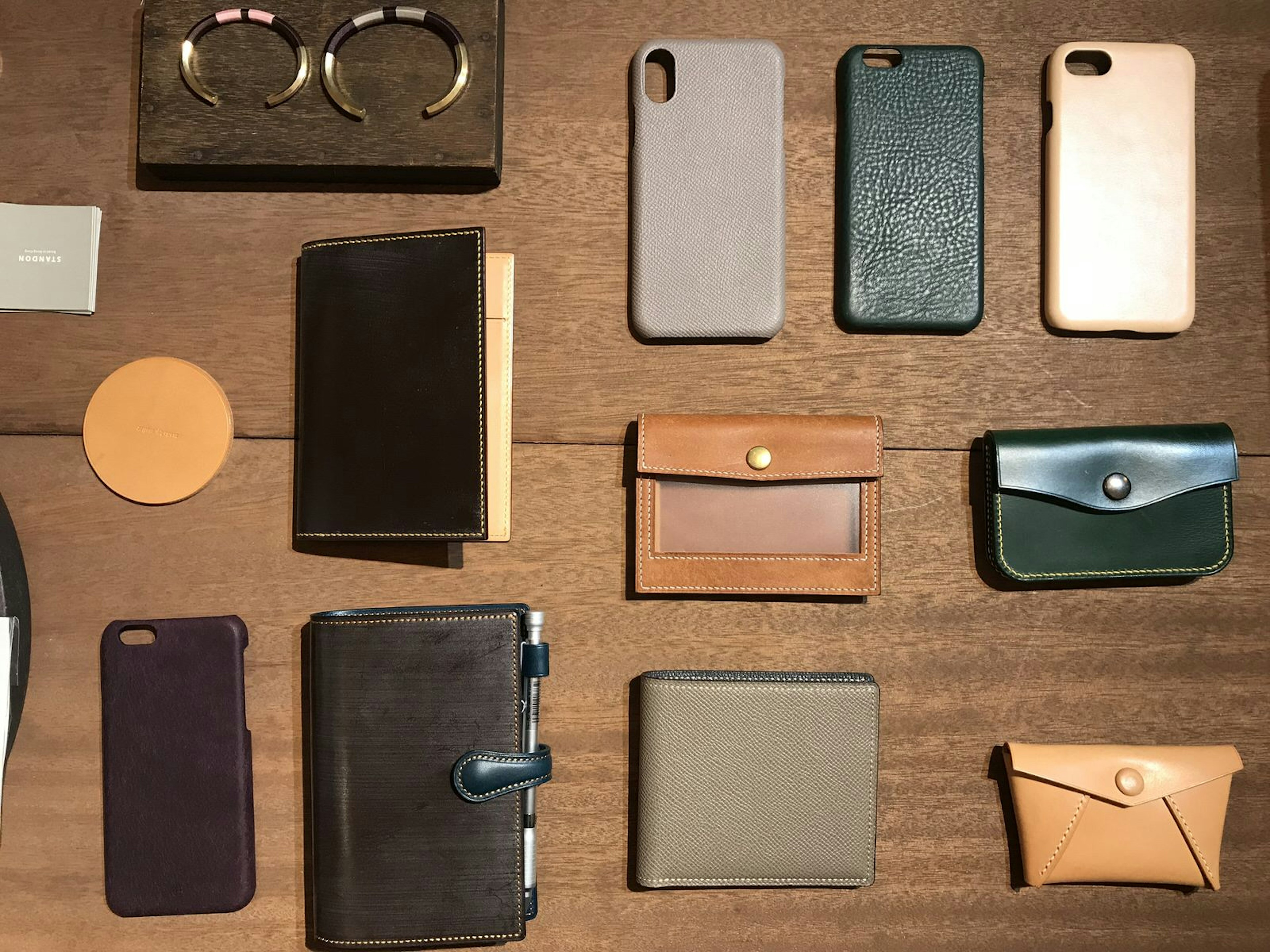 A wooden table displaying a flat lay of leather wallets, phone covers and coin purses