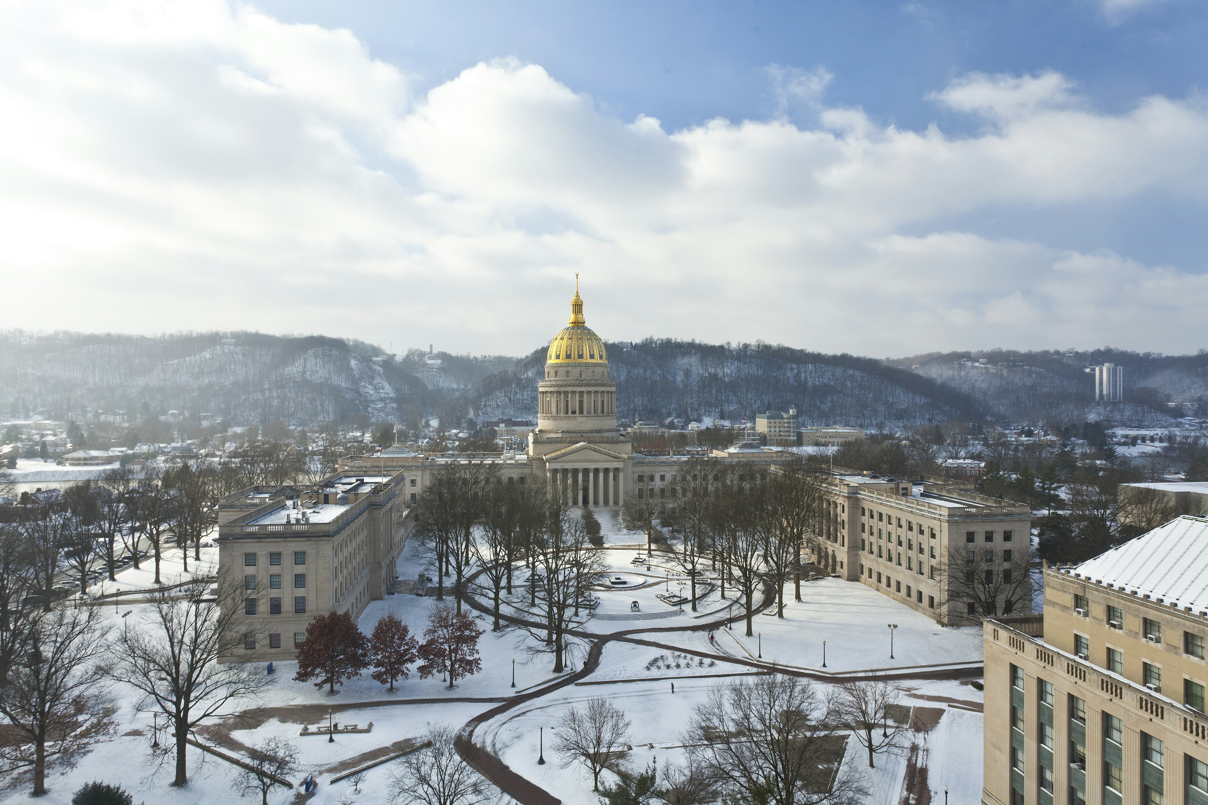 The gold dome of the West Virginia State Capitol building and surrounding campus under a blanket of snow.