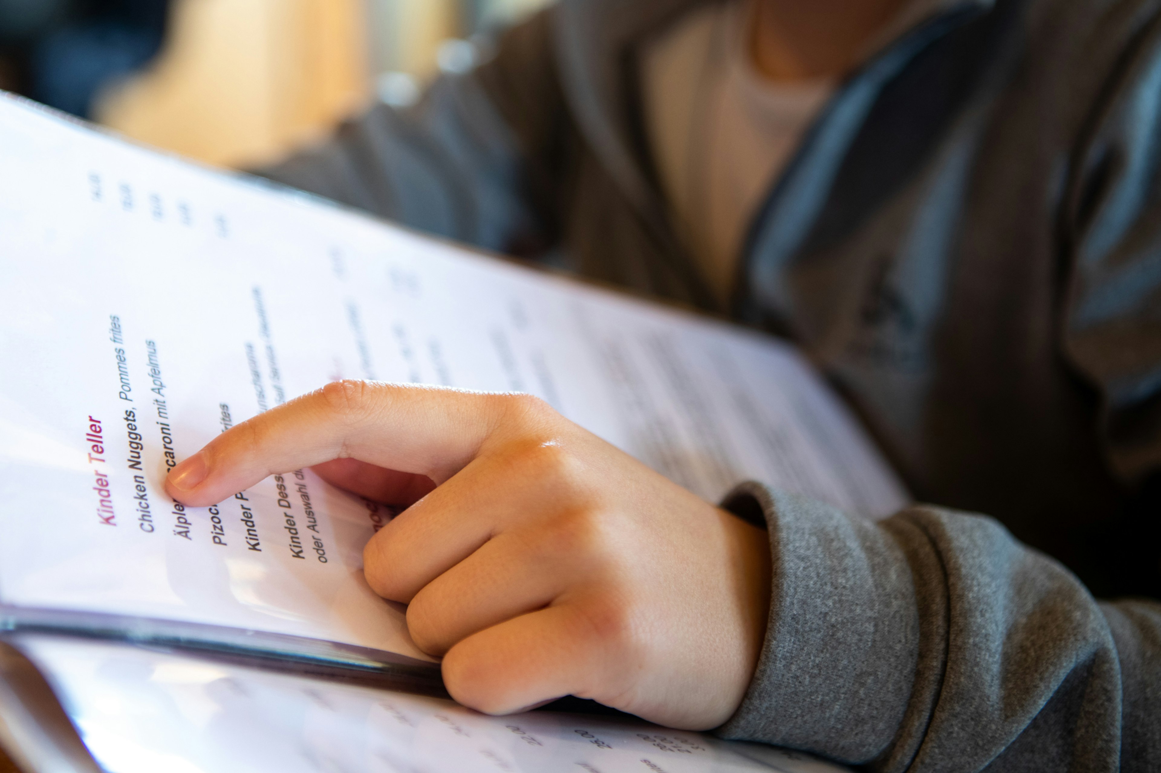 Close-up of a child holding a kids' menu; they are pointing at the first item on the list, which happens to be chicken nuggets.