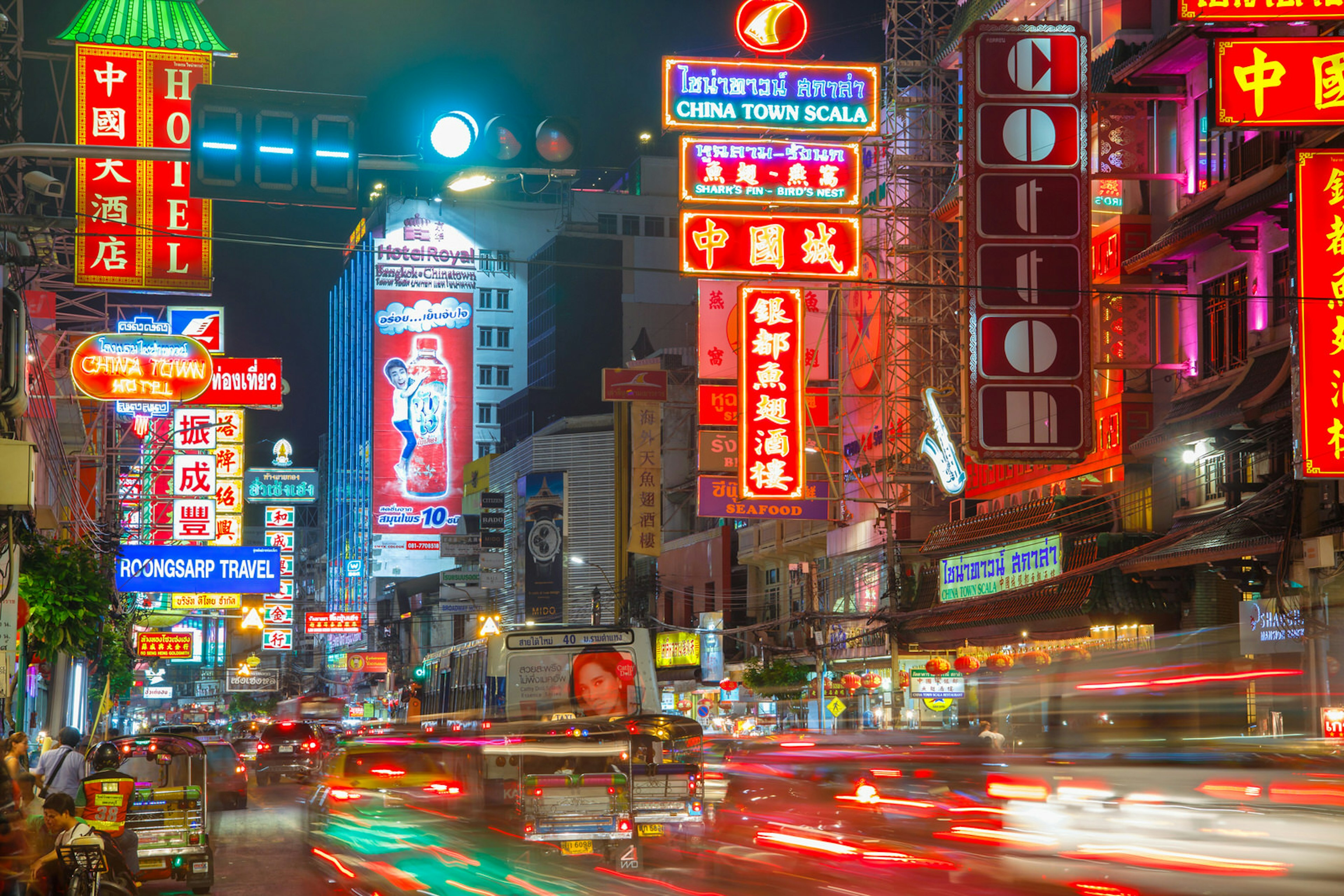 Traffic on Yaowarat Road passes below neon-lit signs in the Chinatown district at night.