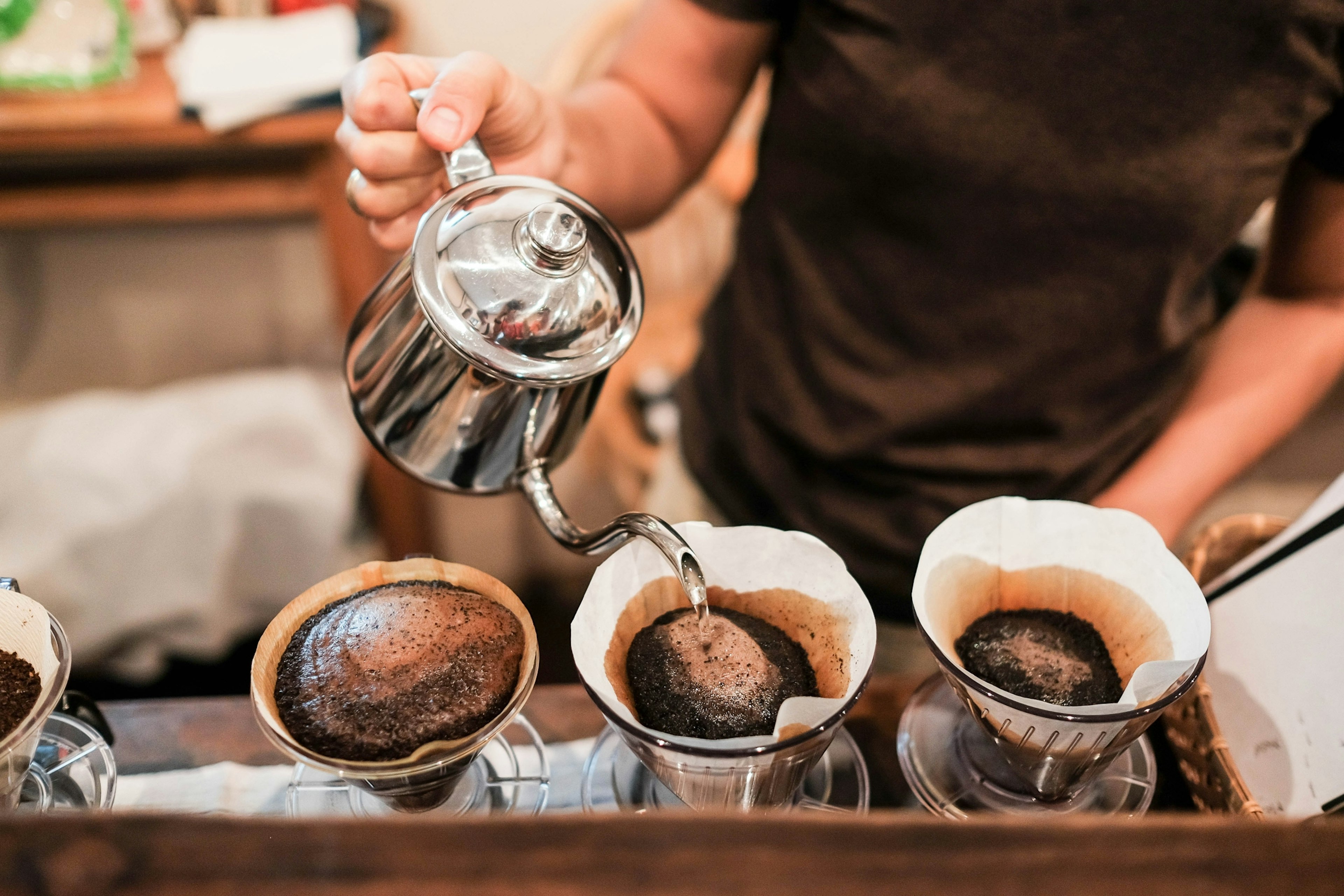 A male barista pour boiling water over ground coffee beans contained in a filter