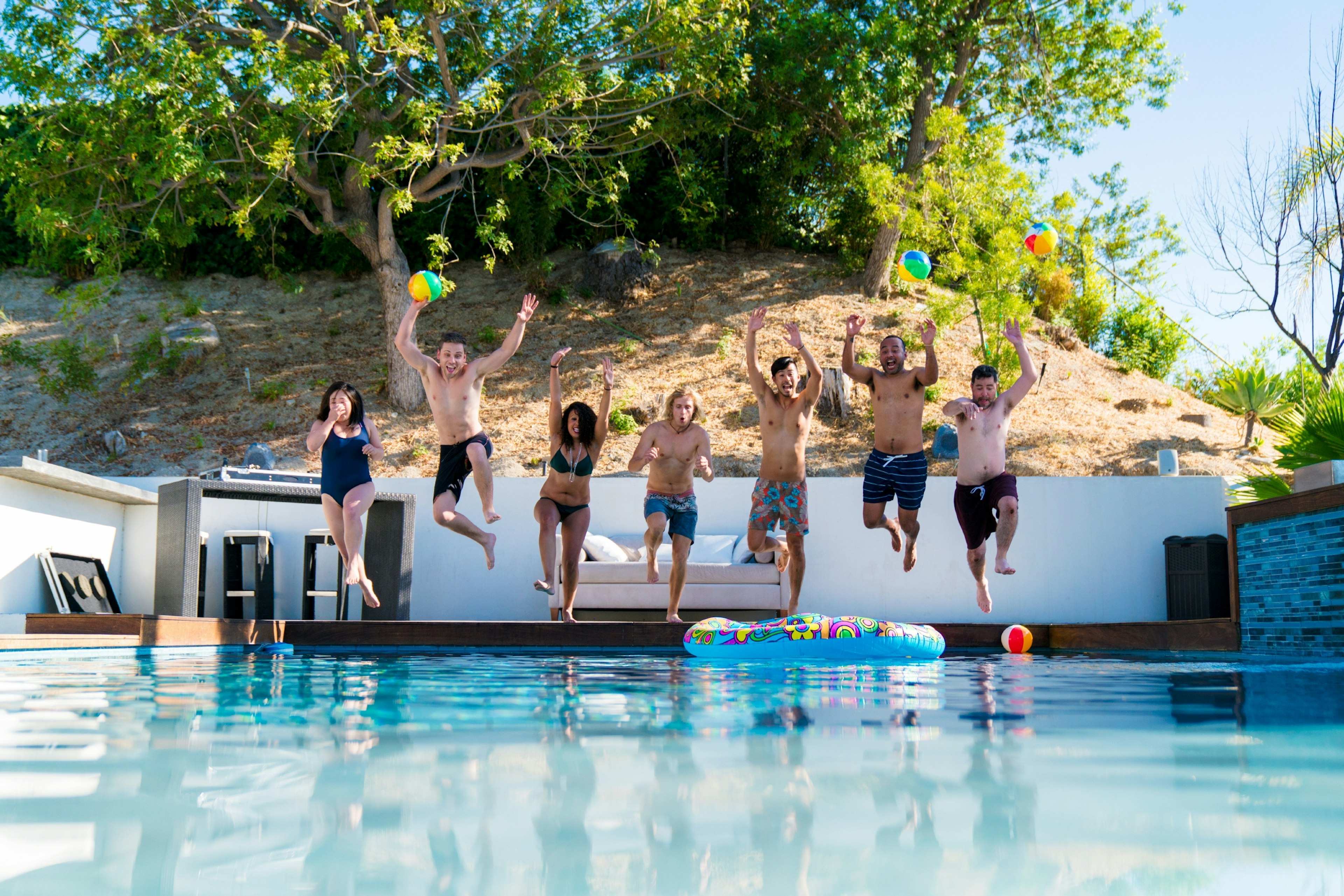 Group of six friends jumping into a swimming pool in Los Angeles on a summer day.