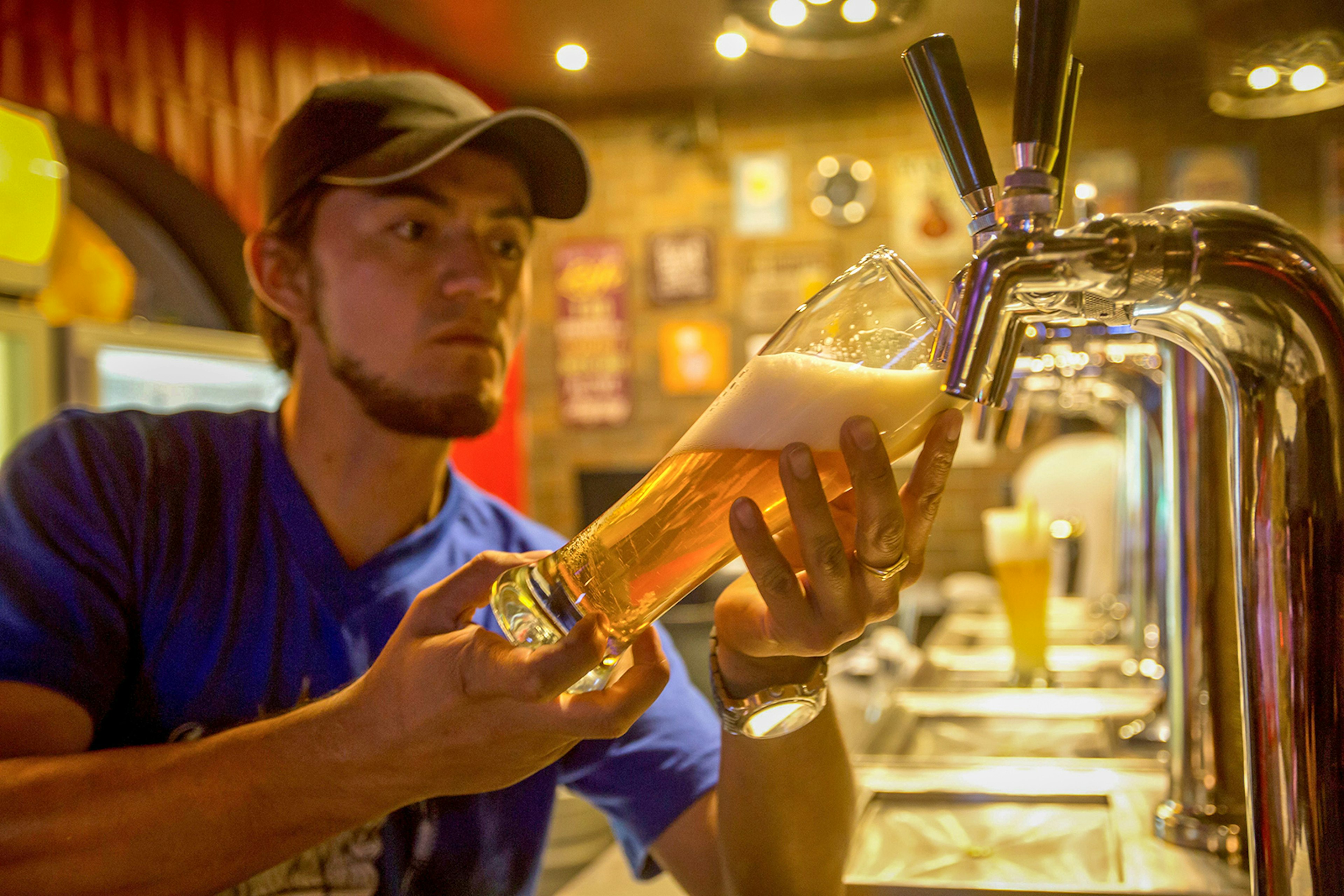 A man pours a beer from a tap in a warm-toned bar setting © JUAN CEVALLOS / Getty Images