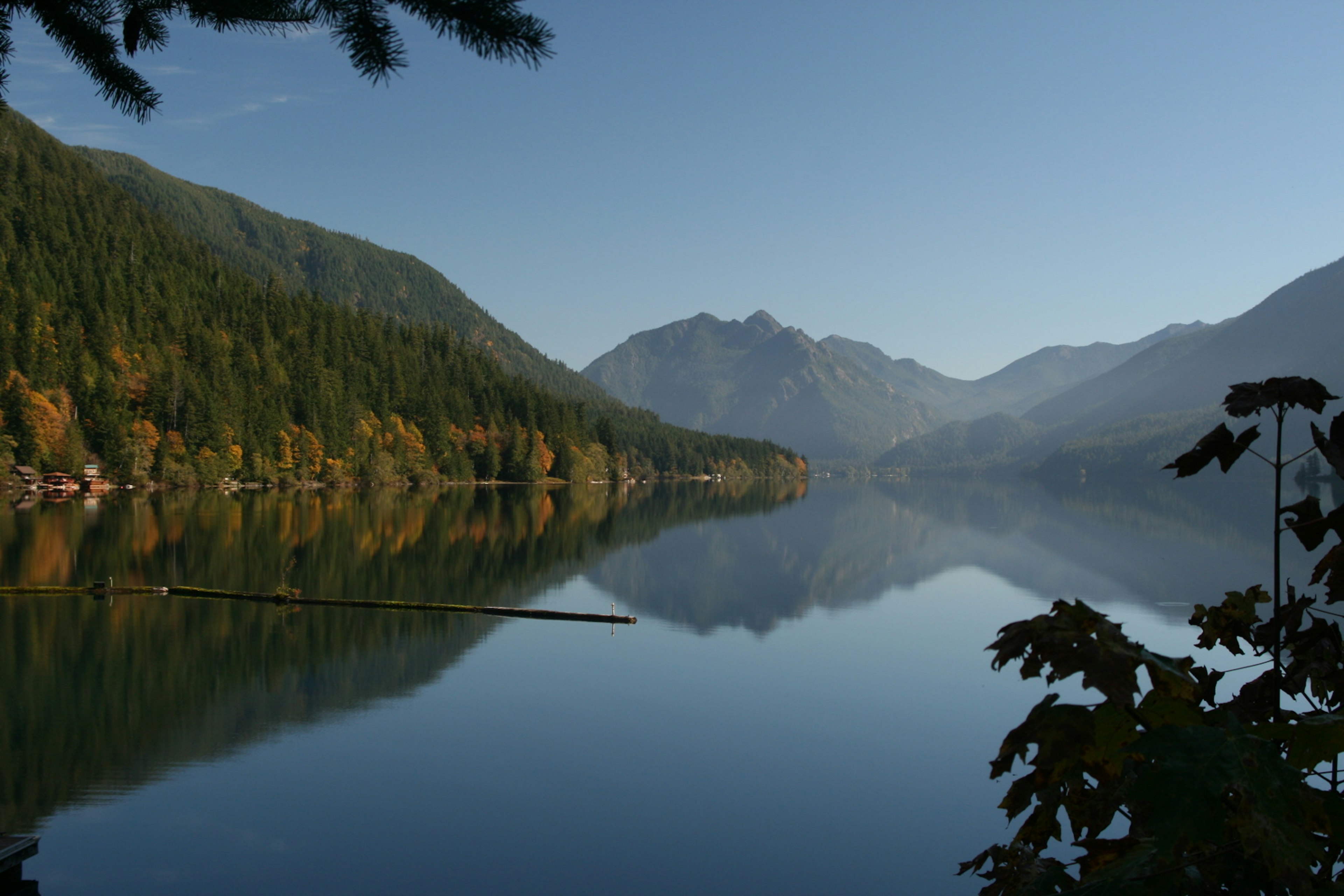 A calm empty lake with mountains all around and reflected in the water.