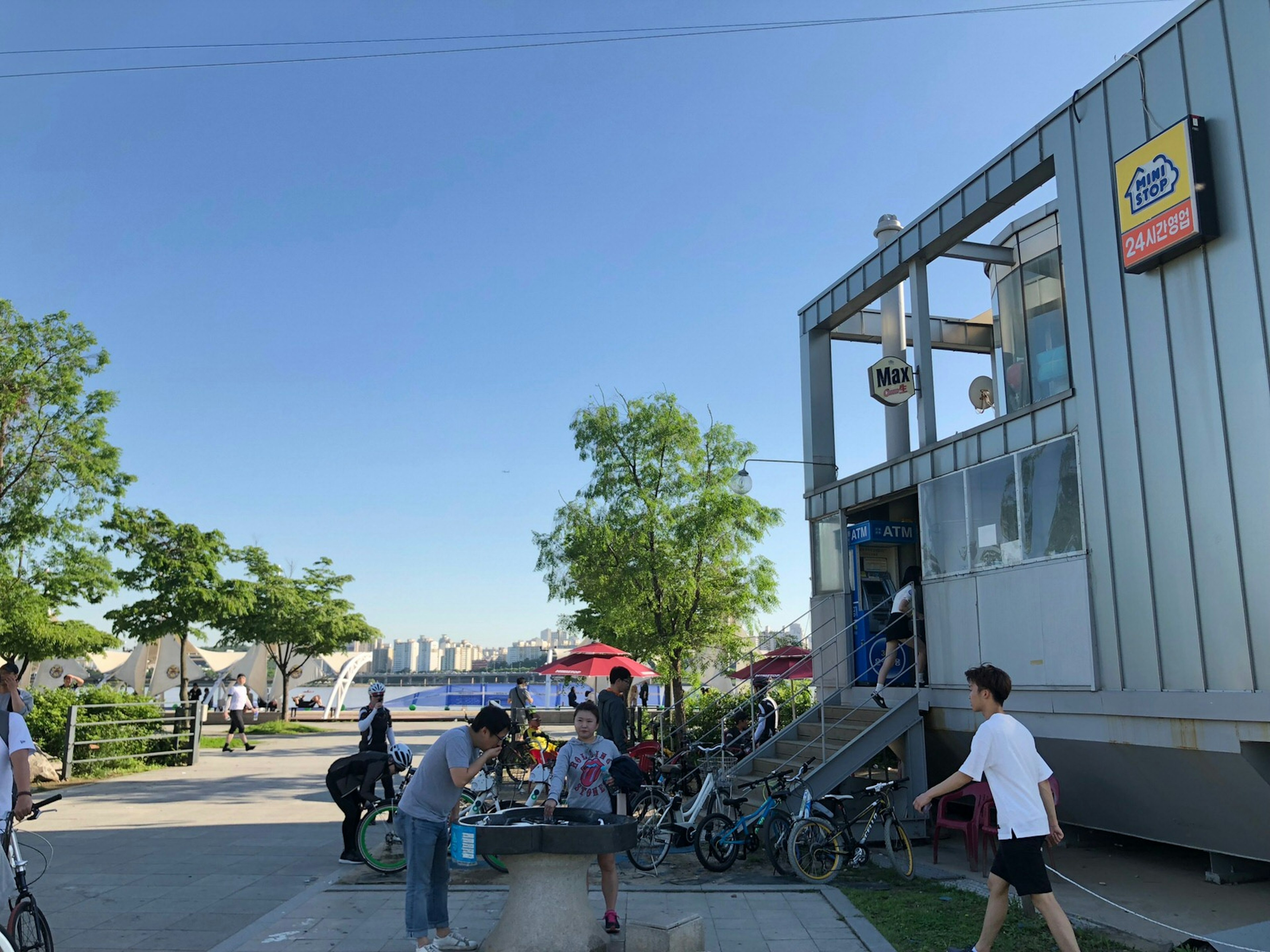 A sunny day with bike parking and some people enjoying the park. This convenience store has views of the Han River © Hahna Yoon / Lonely Planet