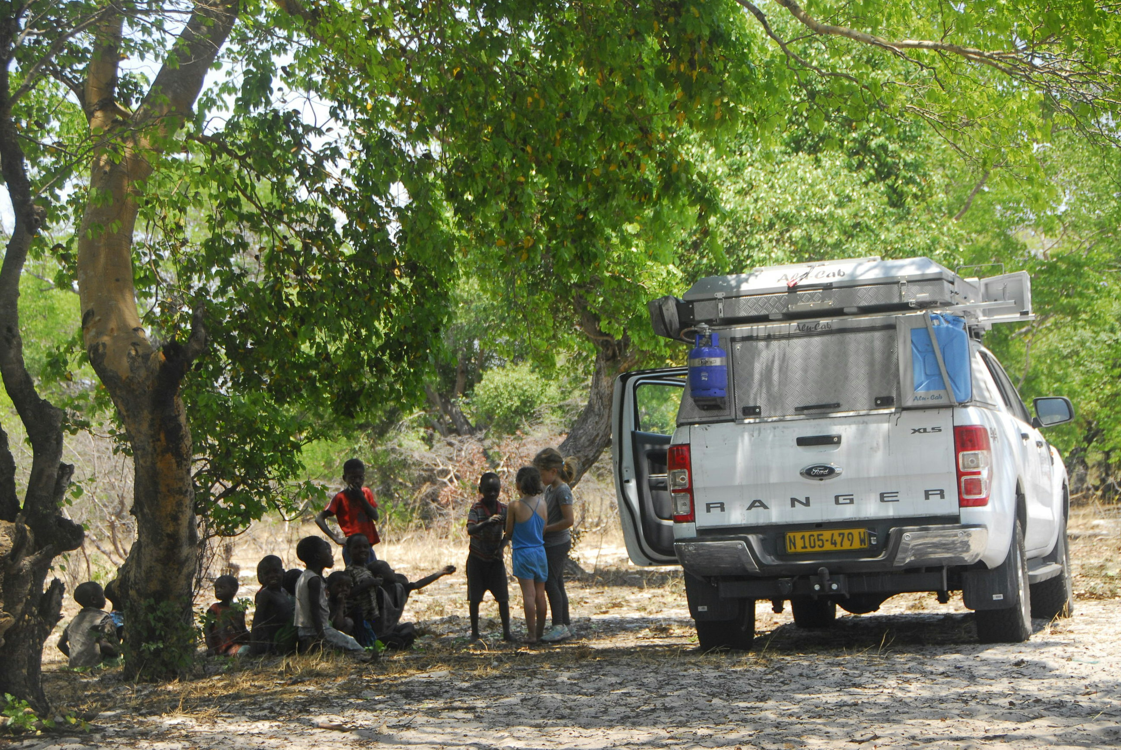 C and V stand next to their dad's vehicle and speak with a group of young children.