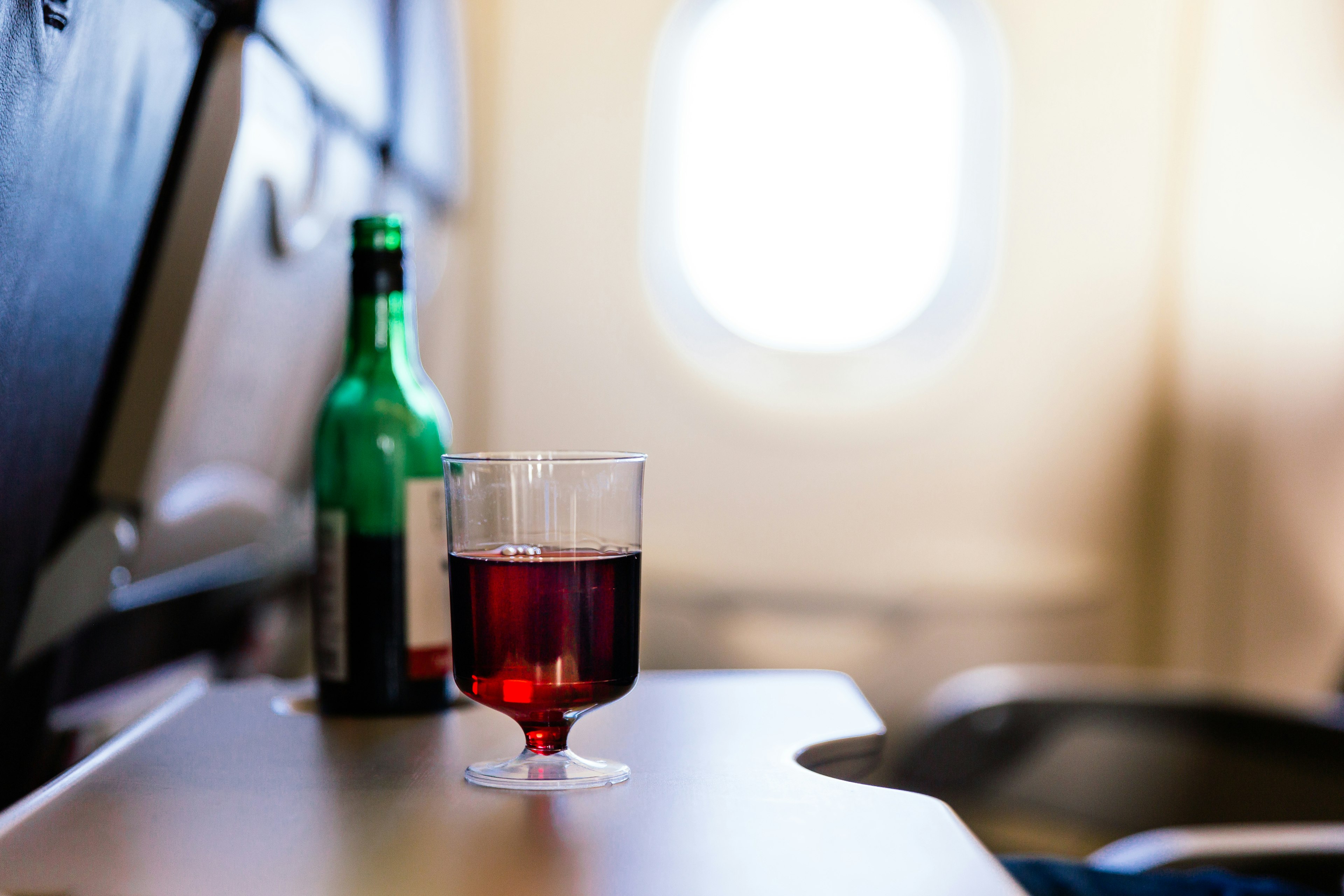 A glass of red wine sits on an airplane tray table.