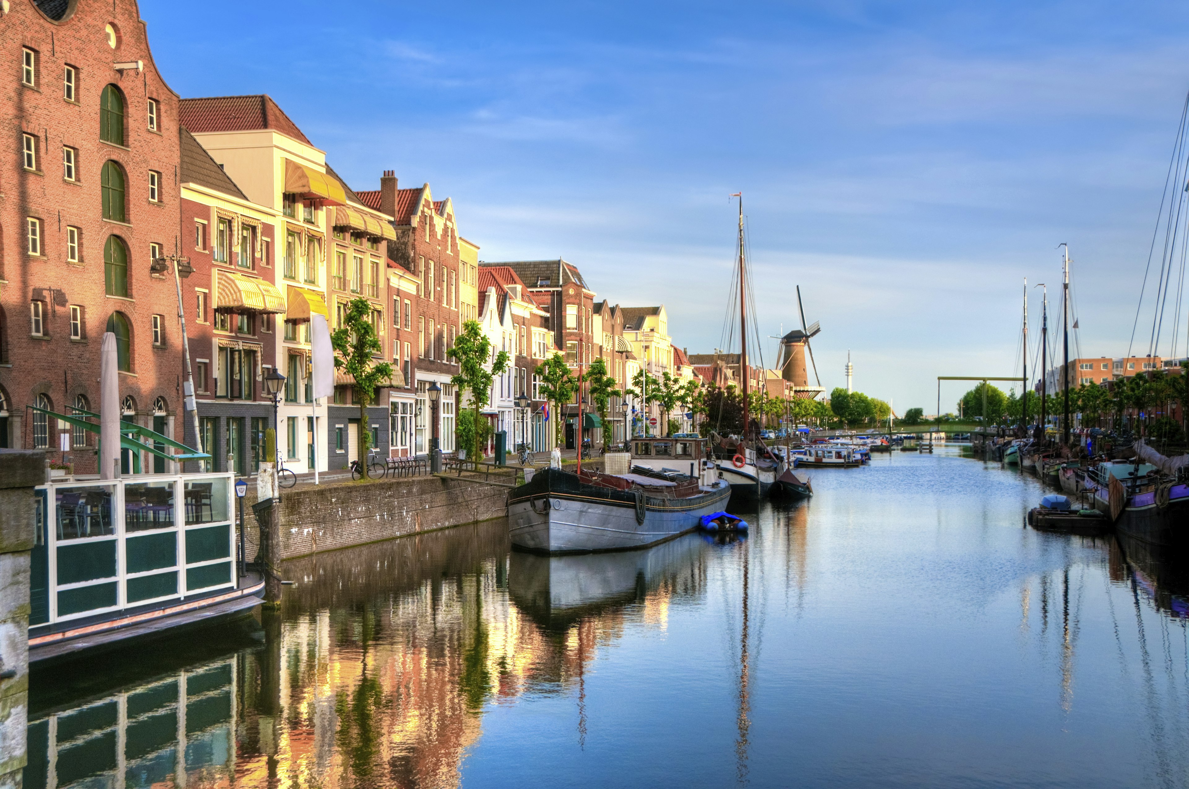 The sun is low over Delfshaven, a pretty harbour in Rotterdam. Old houses line the harbour and many quaint boats are moored.