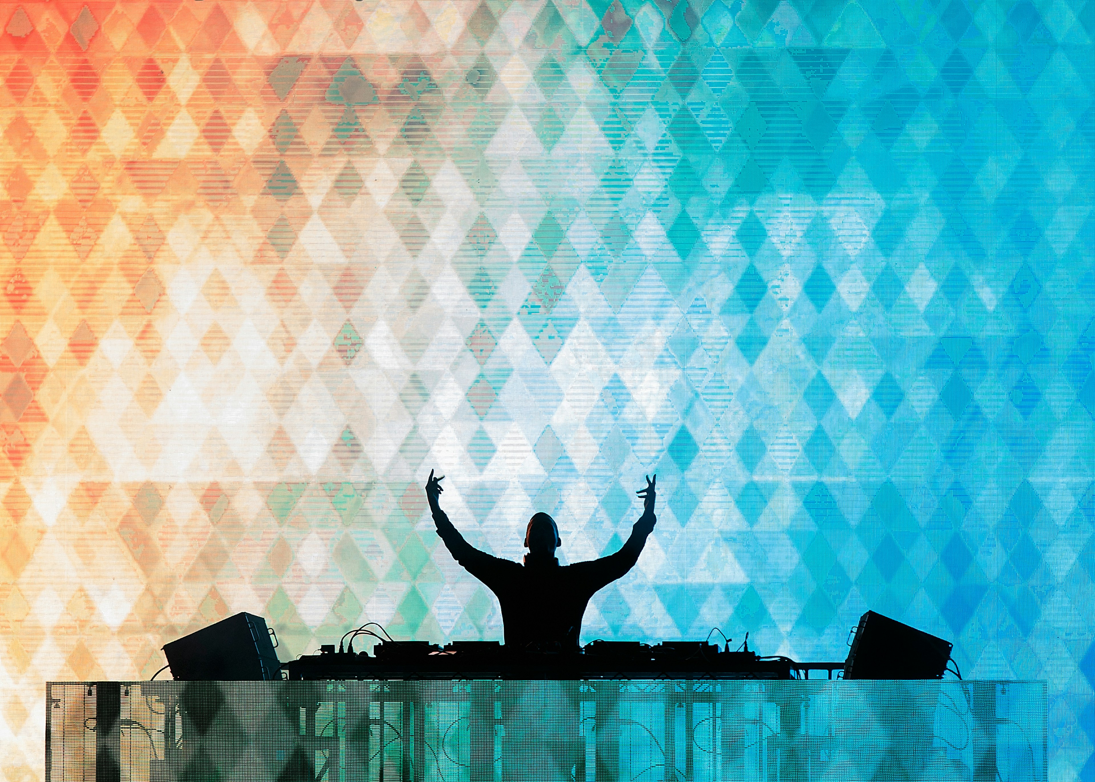 A DJ puts his hands in the air in front of a colorful light display