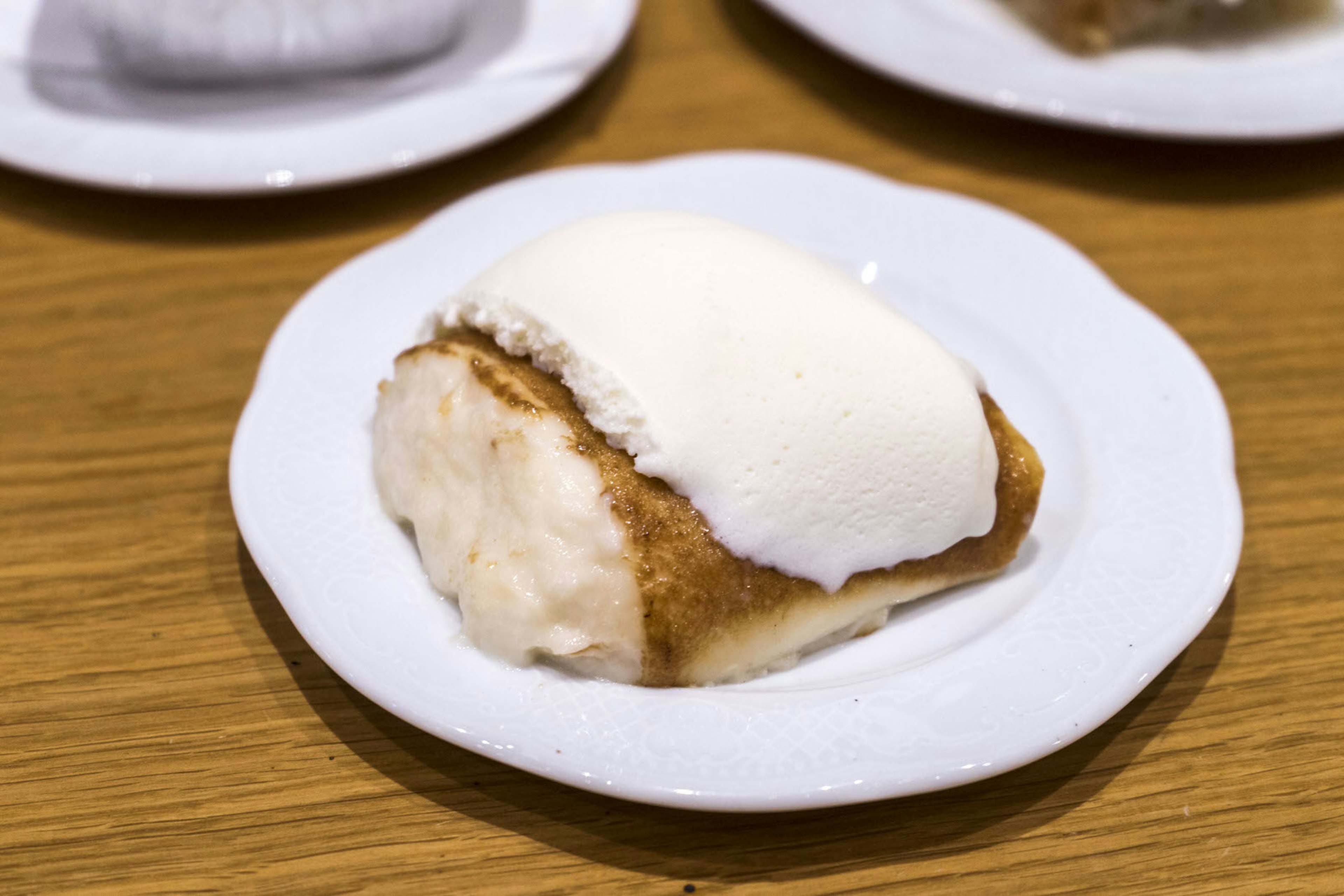 Tavuk göğsü in Turkey, a rice pudding-like dessert made from chicken. The dish is served on a white plate on a wooden table. Levin / Lonely Planet