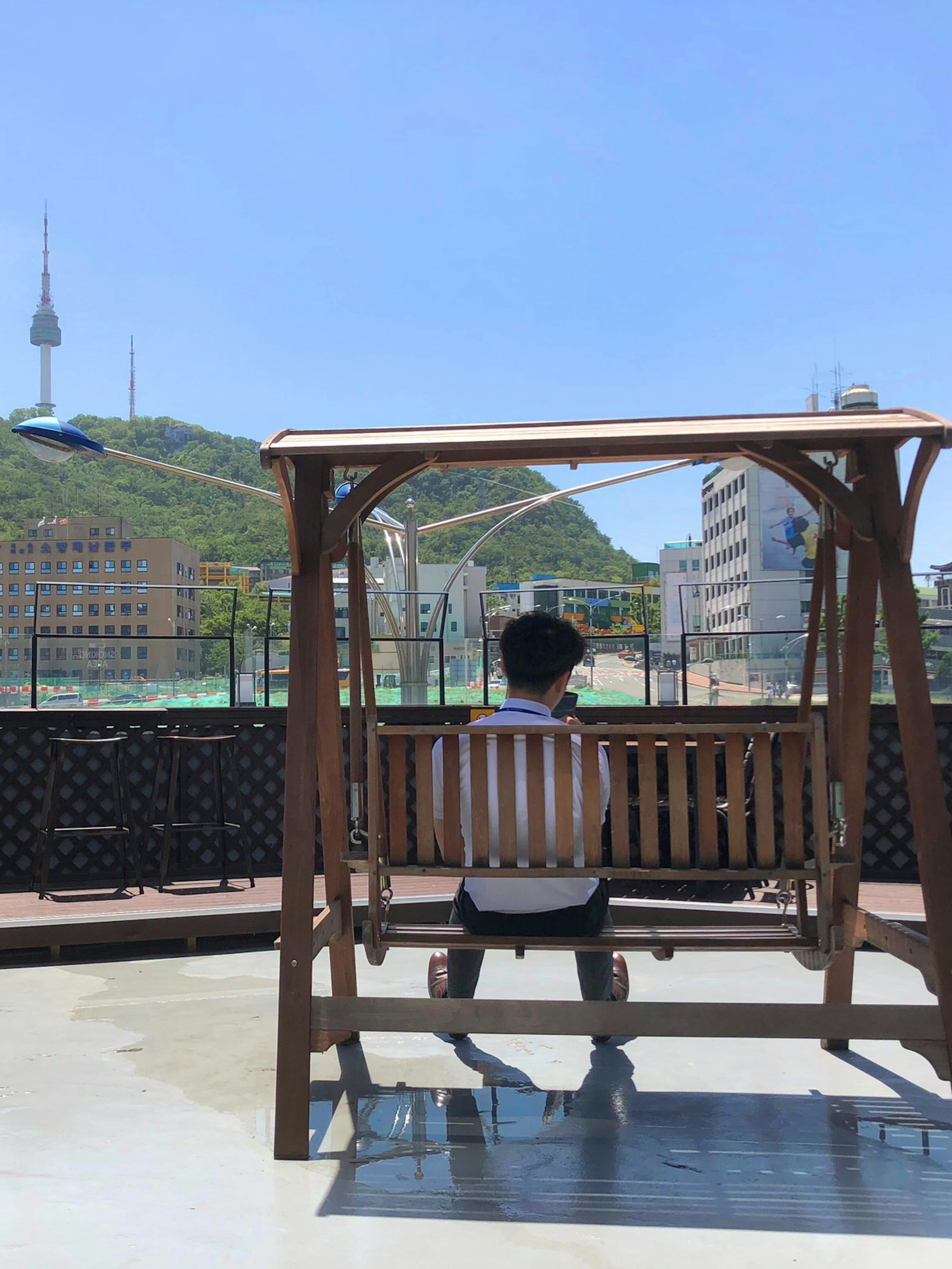 A man sits in a wooden swing on a rooftop overlooking the N Seoul Tower and Namsan. Convenience with a view: this branch of Emart24 has a rooftop overlooking Namsan © Hahna Yoon / Lonely Planet