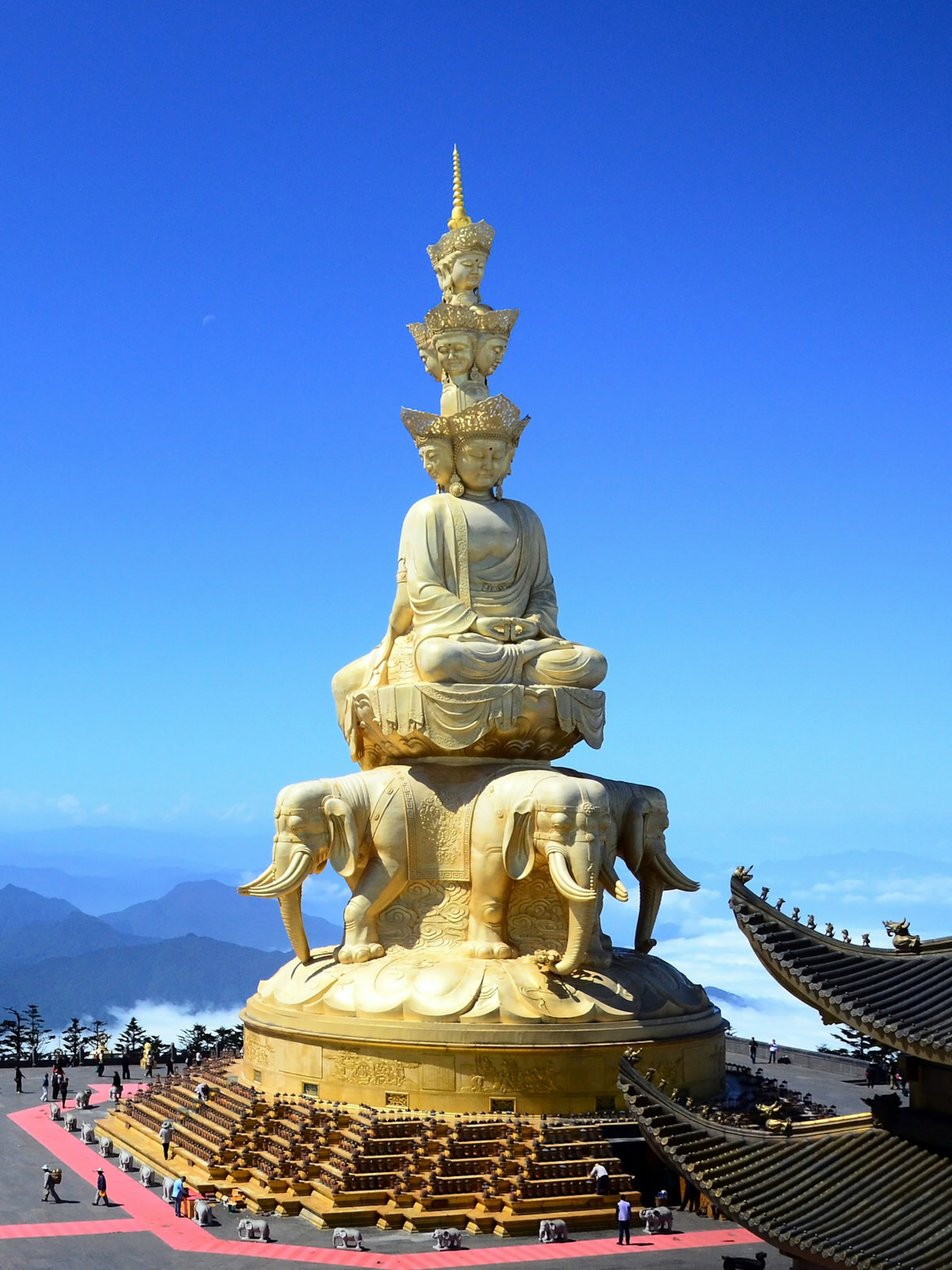 A large golden Buddha statue stands atop a mountain overlooking mountains covered in clouds and mist. The summit of Emei Shan, one of China's four holiest mountains ? M.A.Cynthia / Shutterstock