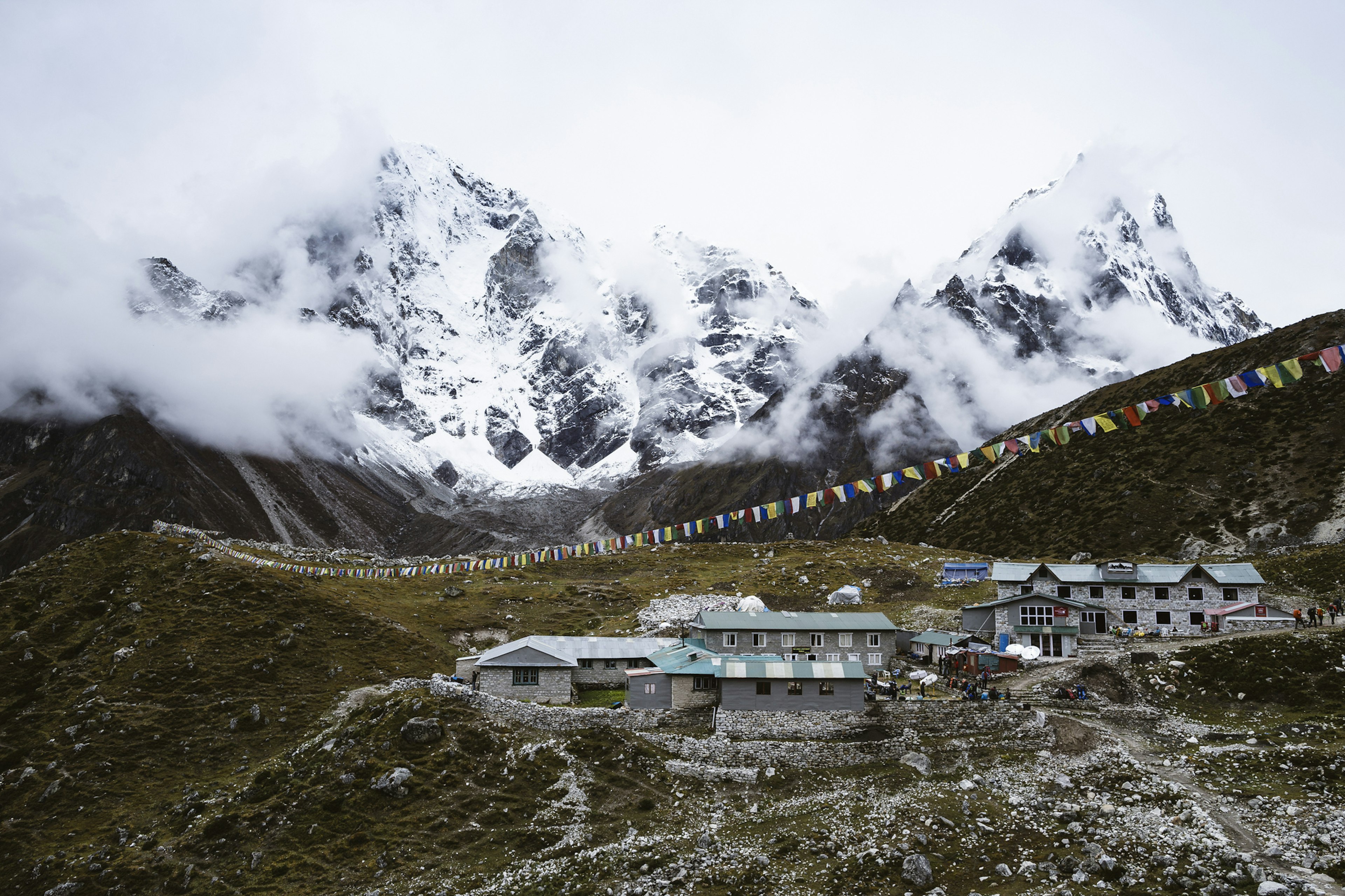 The village of Dughla sits on a rocky outcropping covered in short alpine grass with dramatic Himalayan peaks in the background