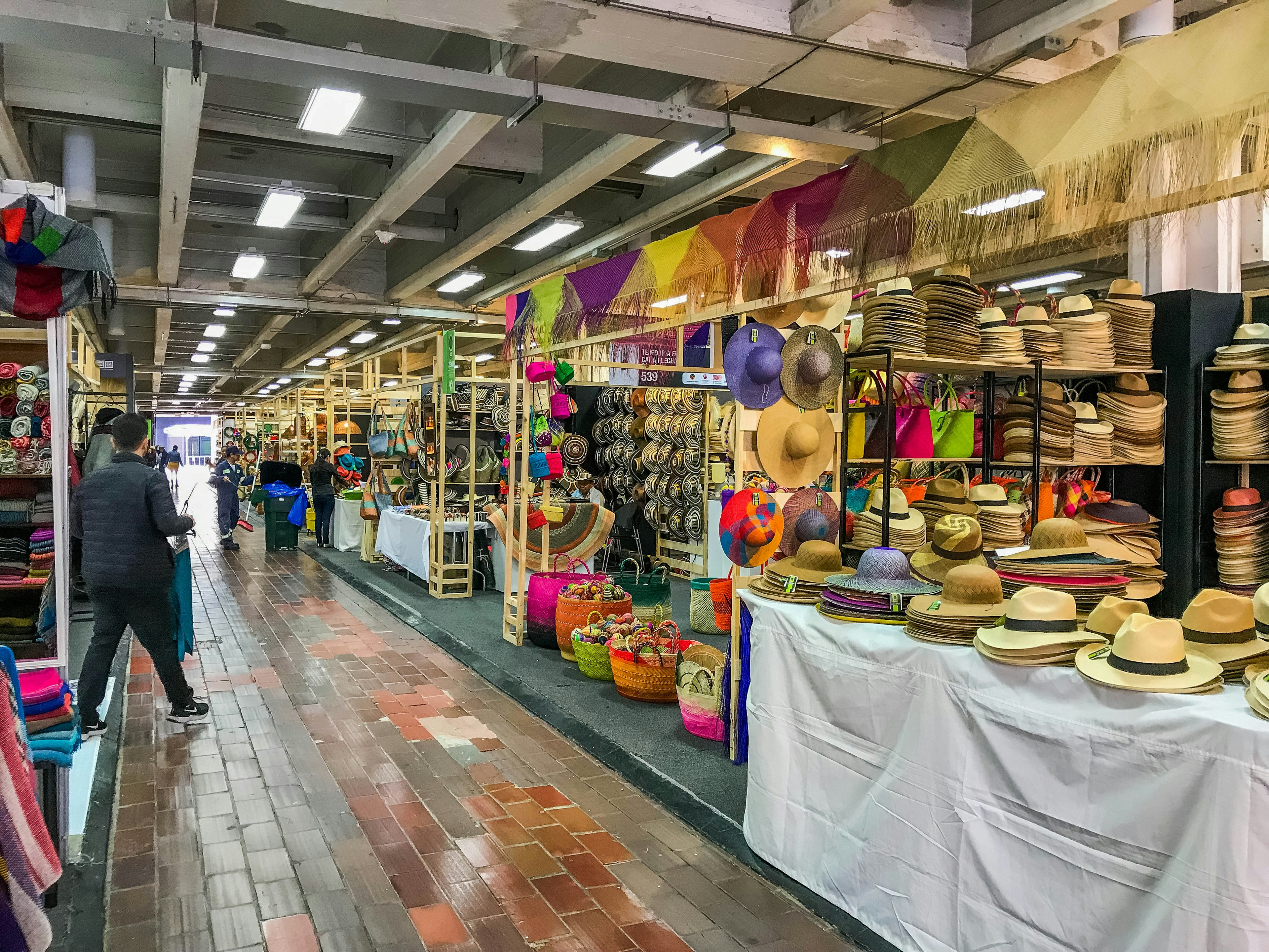 Rows of colorful woven hats, baskets, and other hand-made gifts line the stalls at an indoor market called Expoartesanias