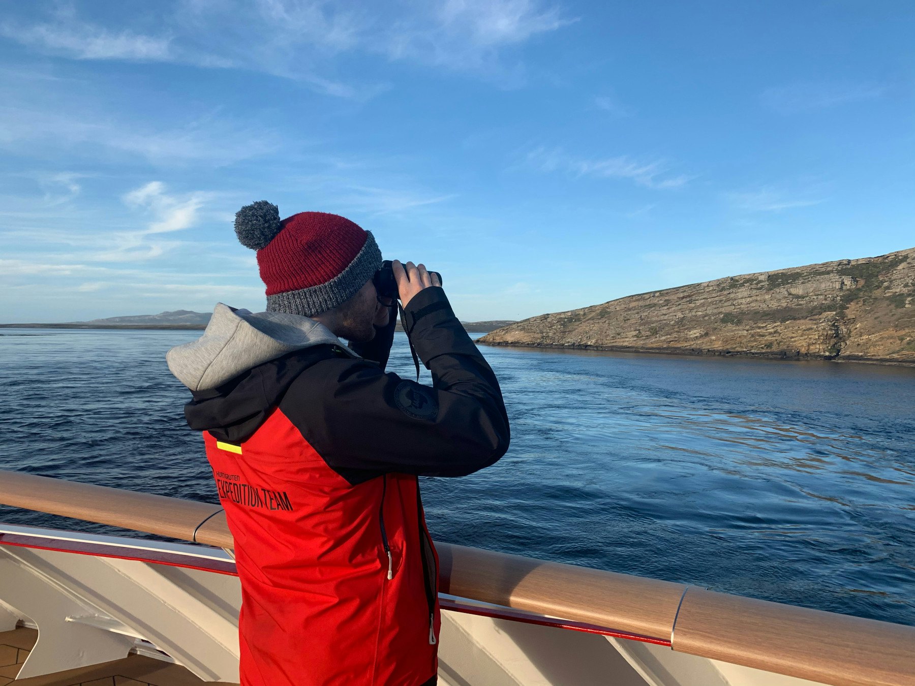 A man looks out from the deck of a ship with binoculars