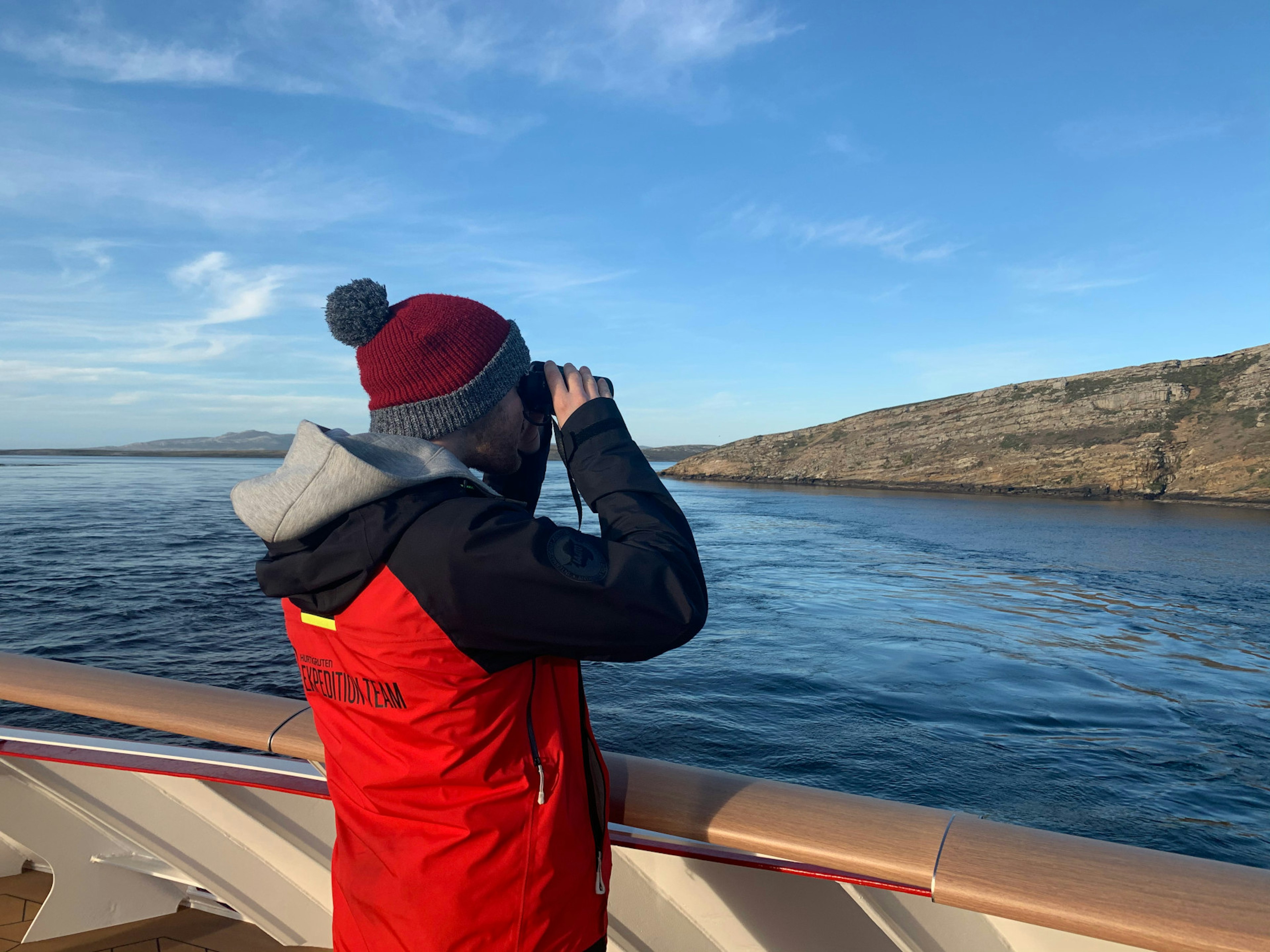 A man looks out from the deck of a ship with binoculars