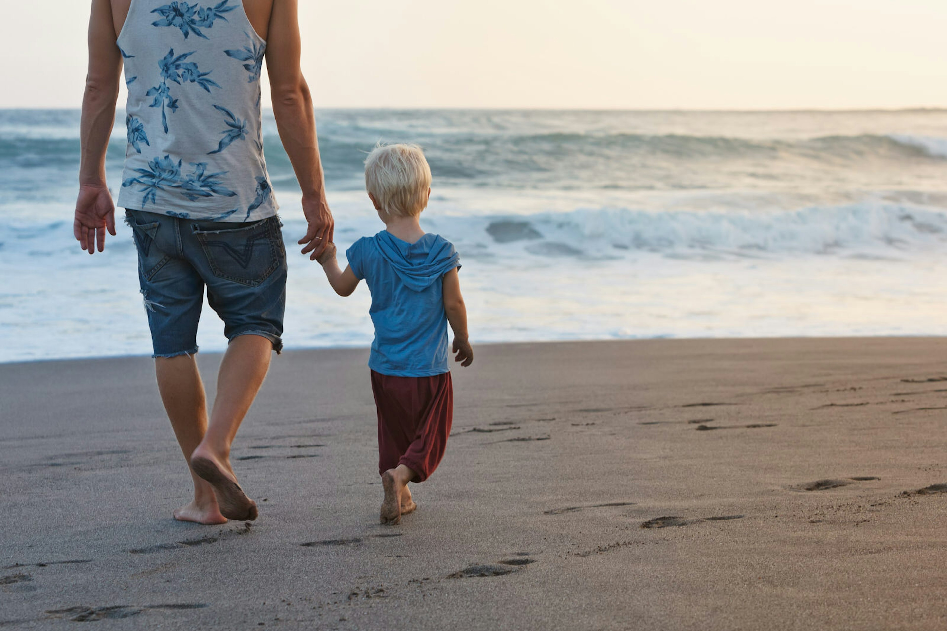 Happy family - barefoot father holds baby son hands, walk with fun along sunset sea surf on black sand beach. Travel, active parents lifestyle, people activity on summer vacations with children.; Shutterstock ID 457792855; Your name (First / Last): Emma Sparks; GL account no.: 61025; Netsuite department name: Online Editorial; Full Product or Project name including edition: Road trip with kids article