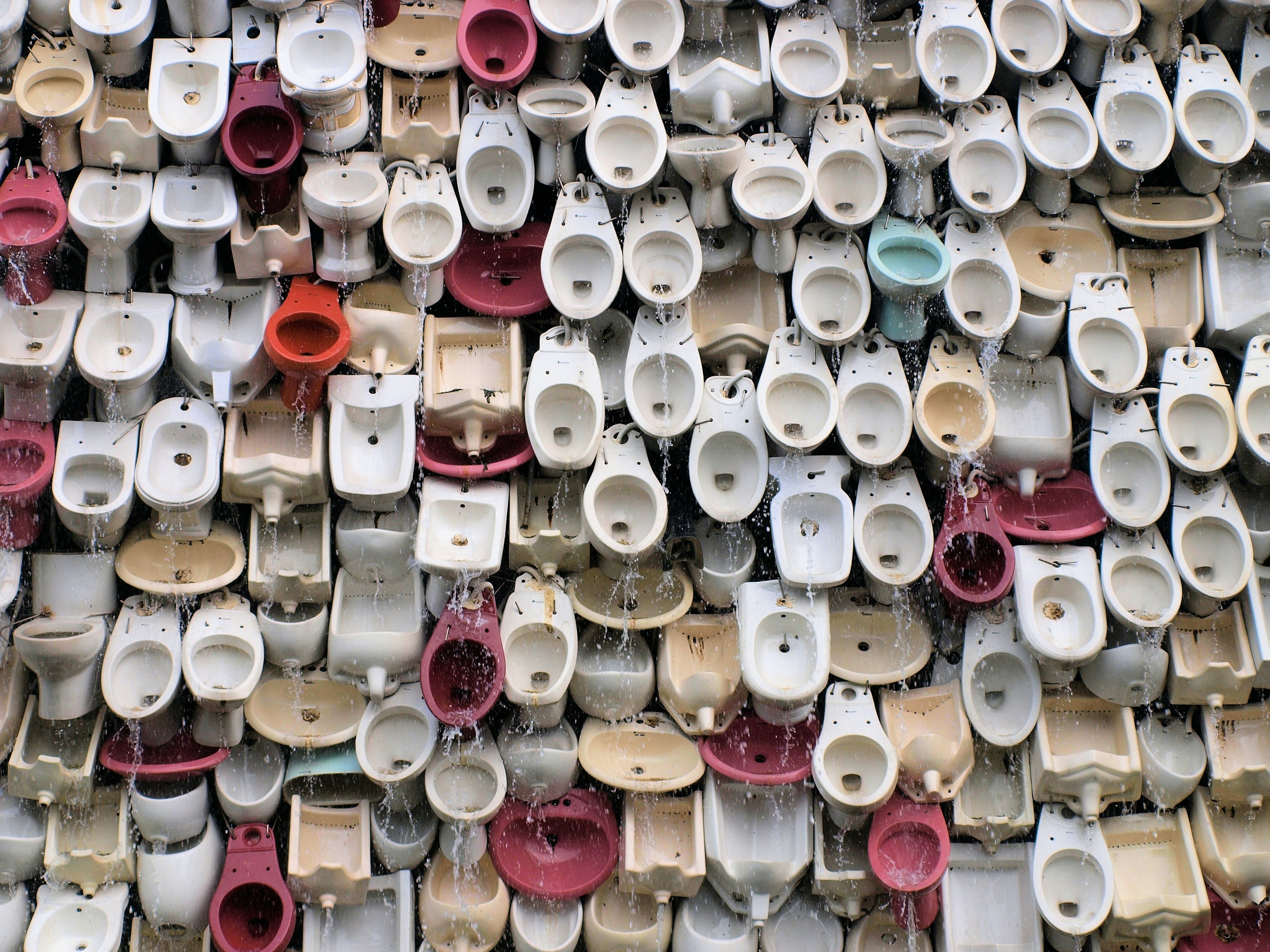 A flat, compressed image of a full wall of toilets, water cascading down the toilets in the style of a waterfall.