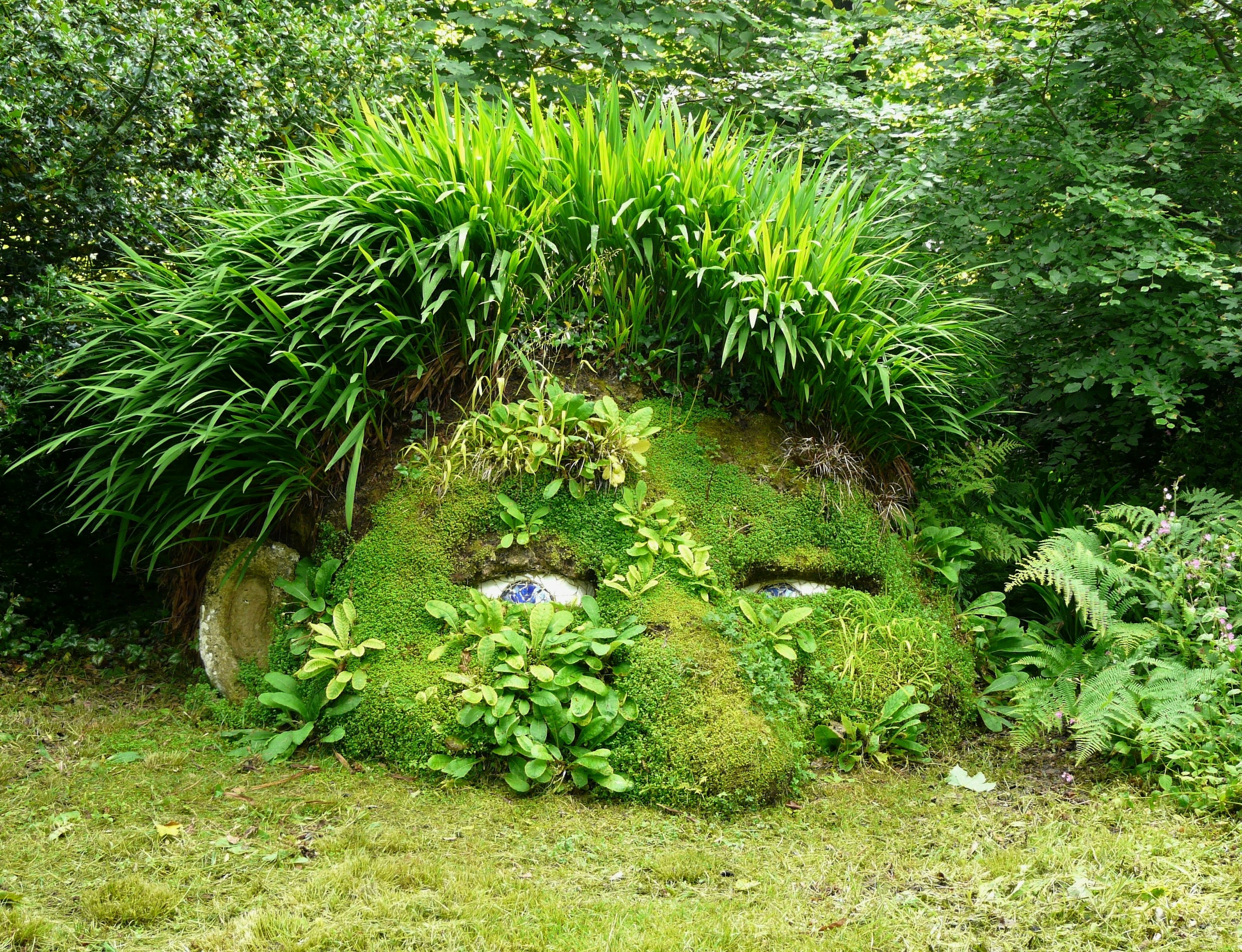 A sculpture in the shape of a half-buried giant's head covered in plants