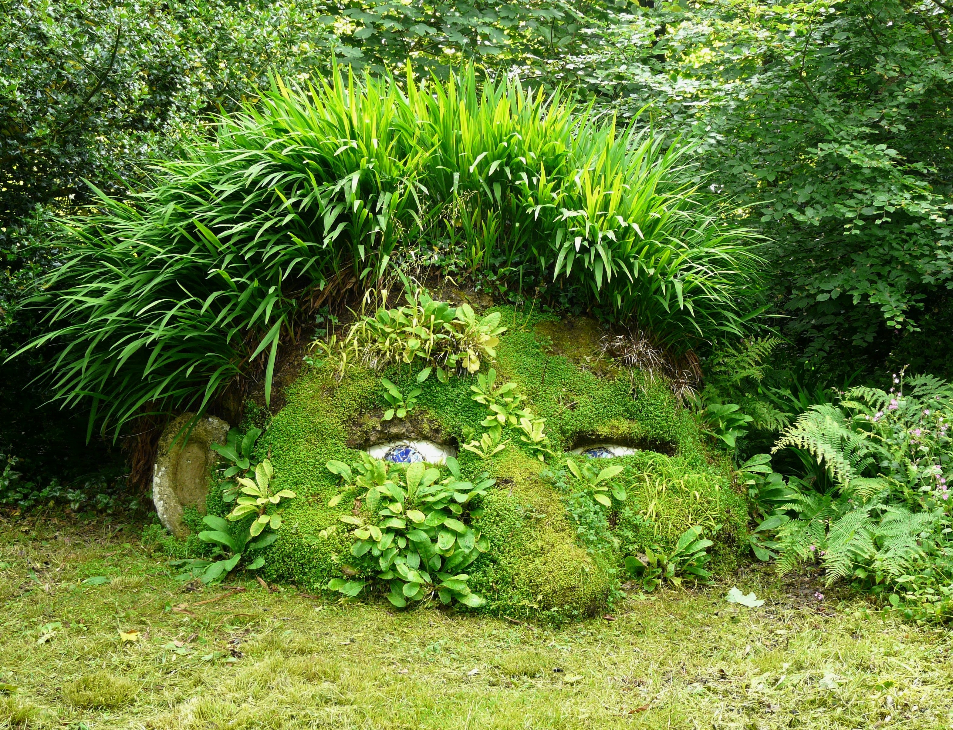 A sculpture in the shape of a half-buried giant's head covered in plants