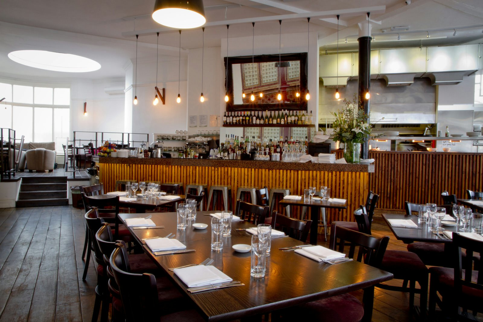 The elegant interior of The Gate, with dark wood tables and chairs, white walls, and bare bulbs hanging over a bar that's loaded with drinks.