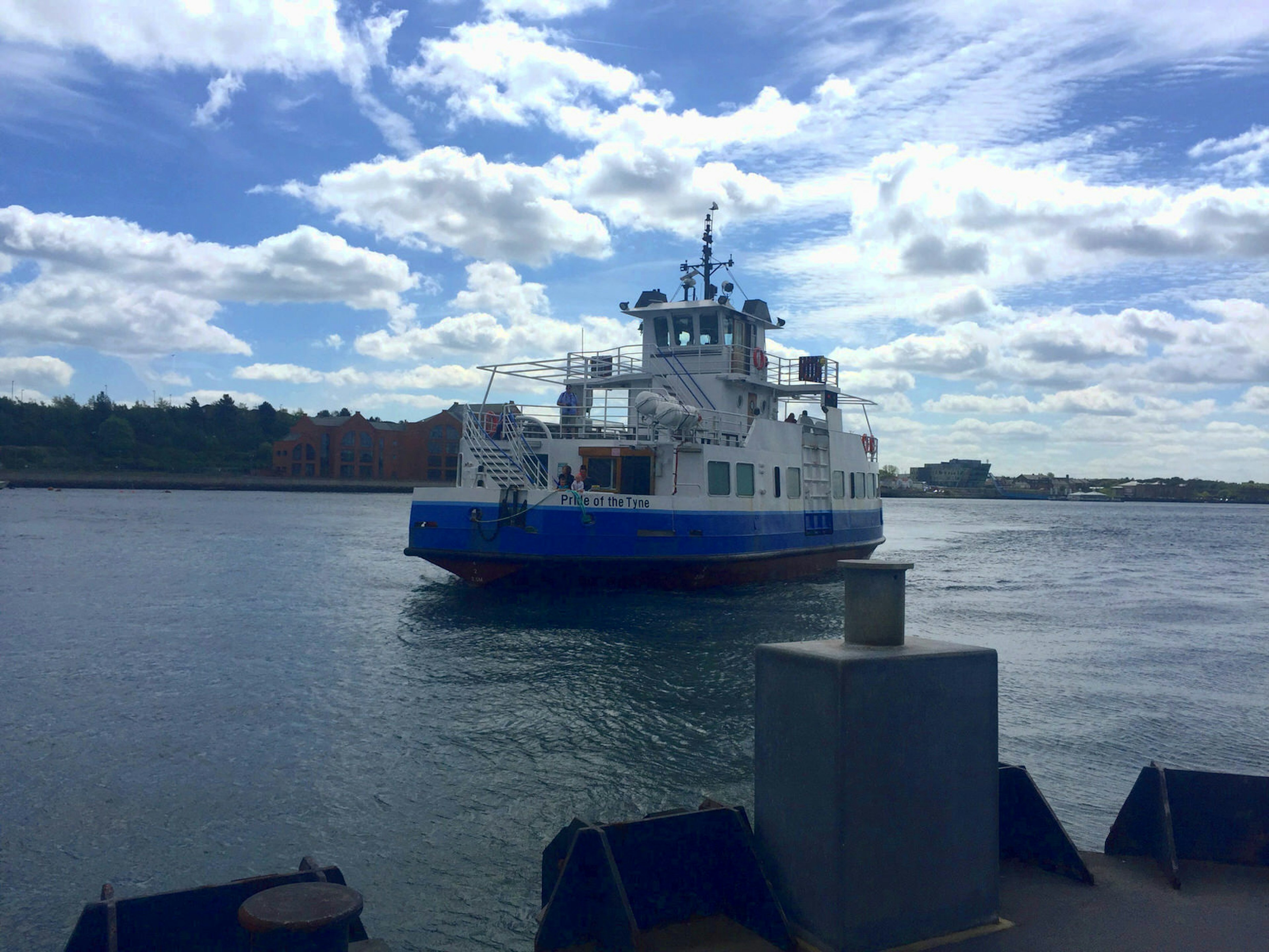 A white and blue boat leaving dock and crossing the River Tyne