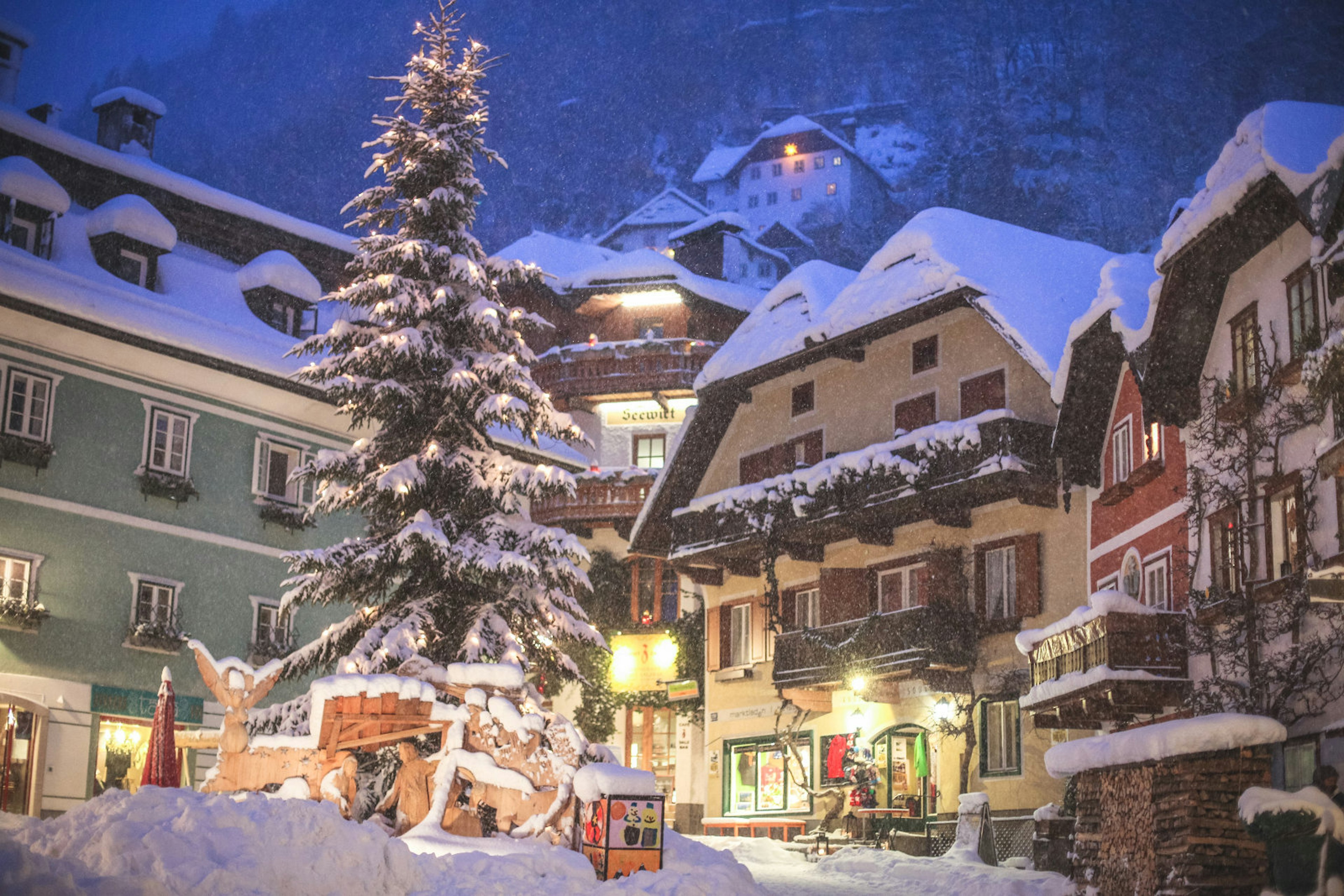 The town square under snow. In the centre is a Christmas tree with big presents underneath.