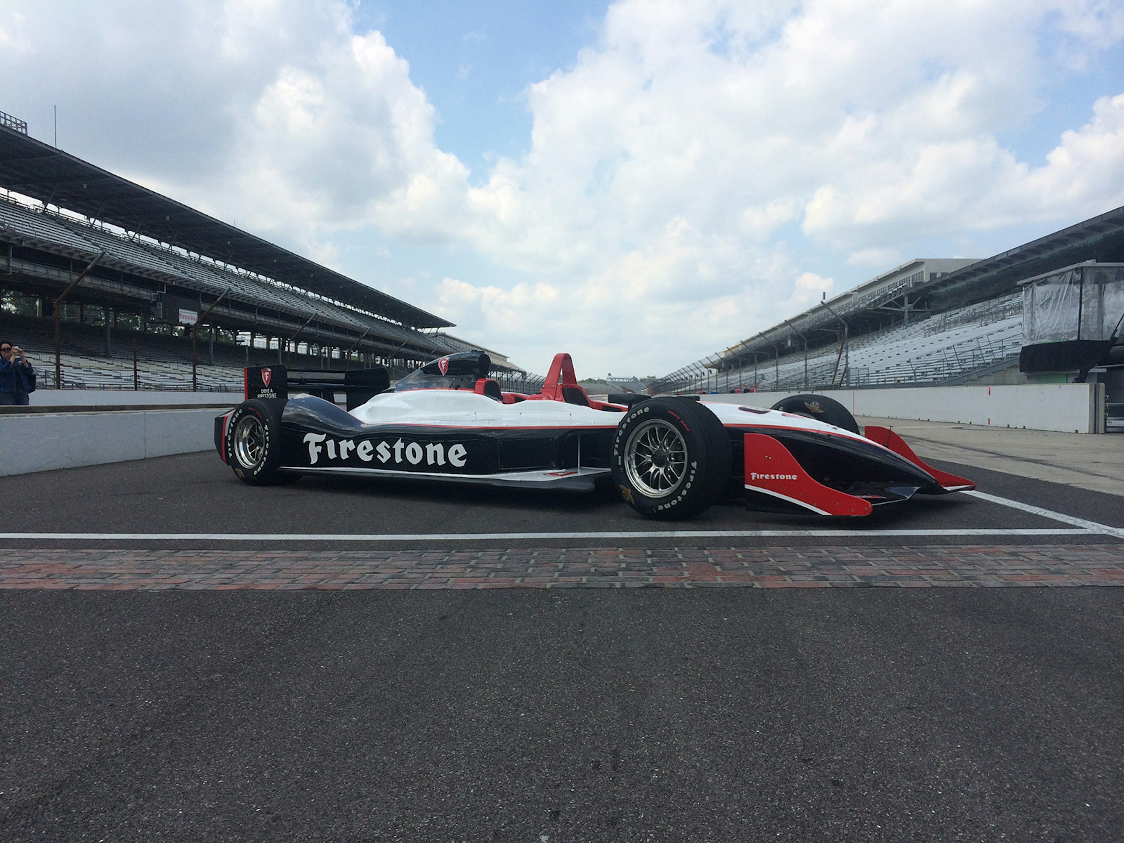 wide shot of an IndyCar with the Indianapolis Motor Speedway in the background and the yard of bricks in the foreground © IndyCar Experiences