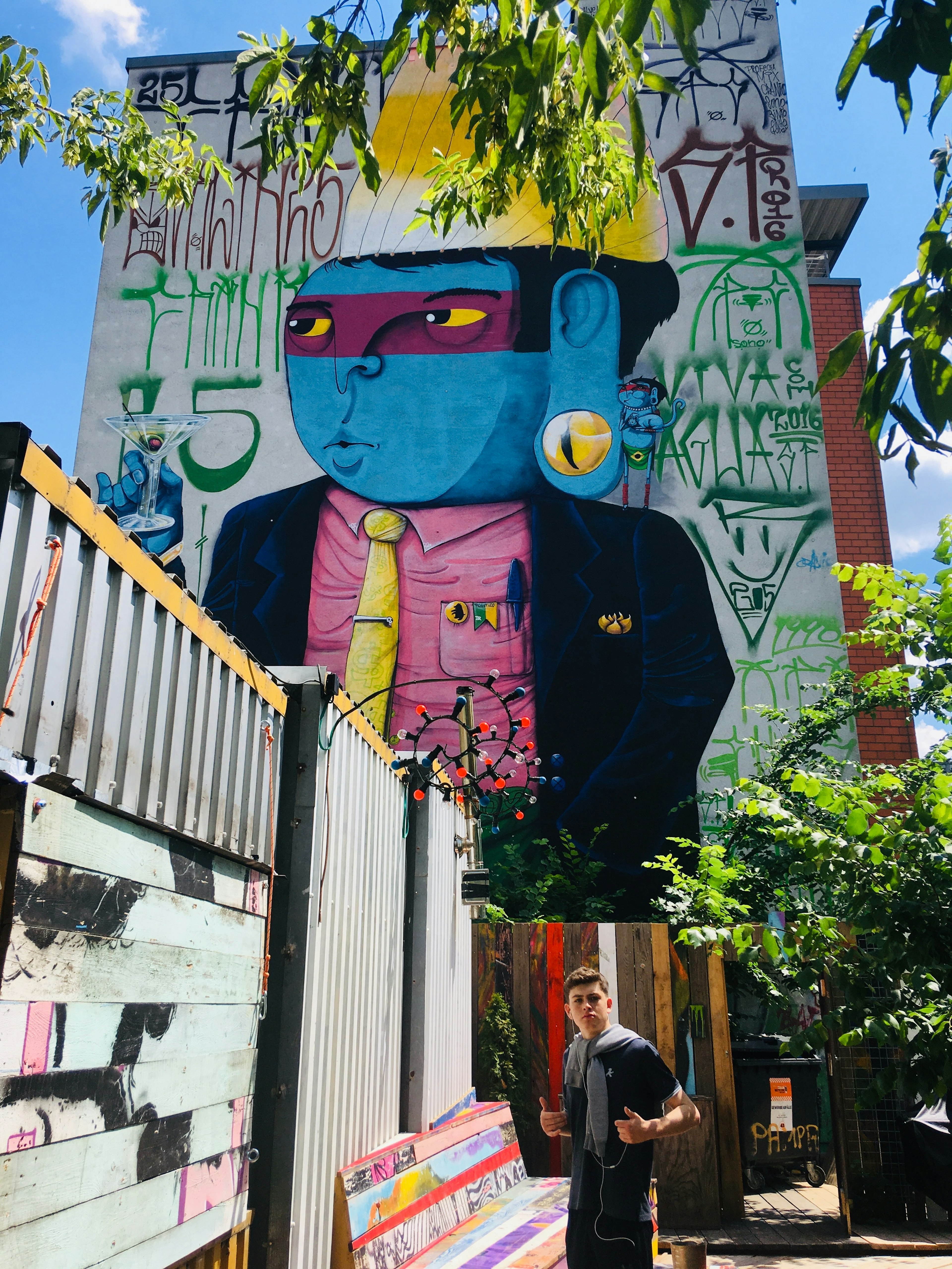 Rhonda Carrier's teenage son, Ethan, stands in front of a huge mural of a cartoon man in Holzmarkt, Berlin.