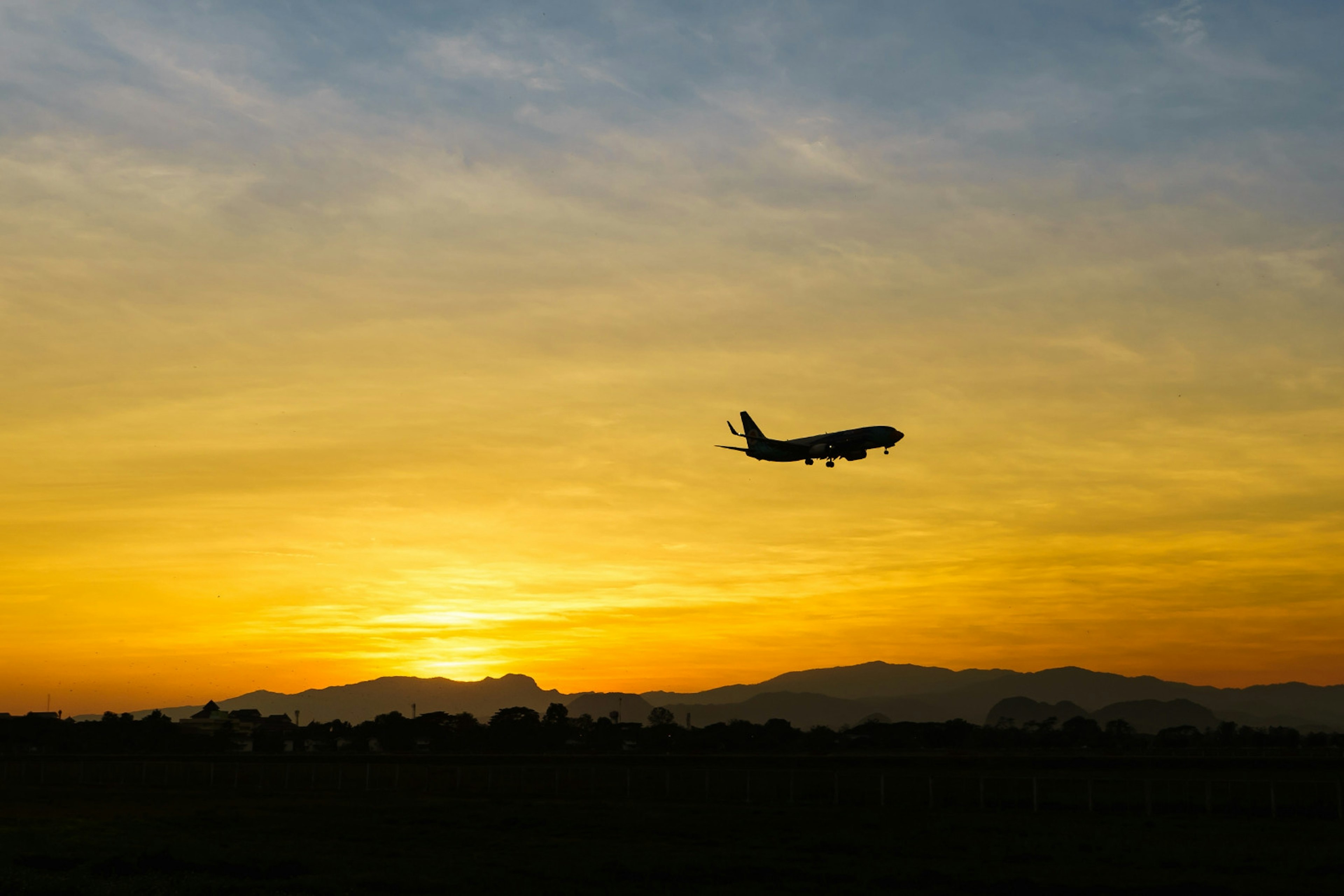 An orange and yellow horizon with a silhouette of a plane flying in the sky.