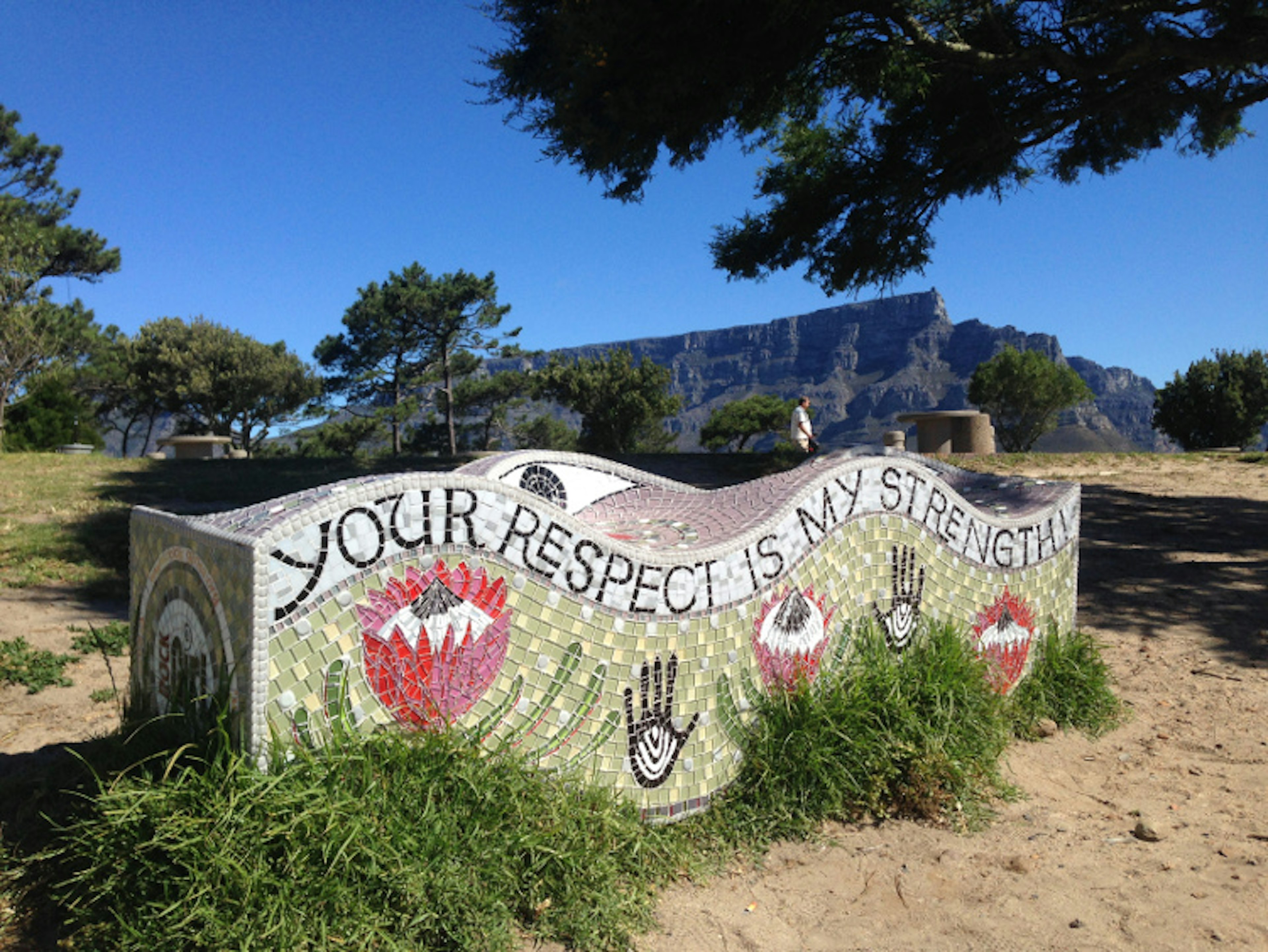 A large bench covered in a mosaic of tiles that read 'your respect is my strength'; the shape of the bench is undulating like a rolling wave