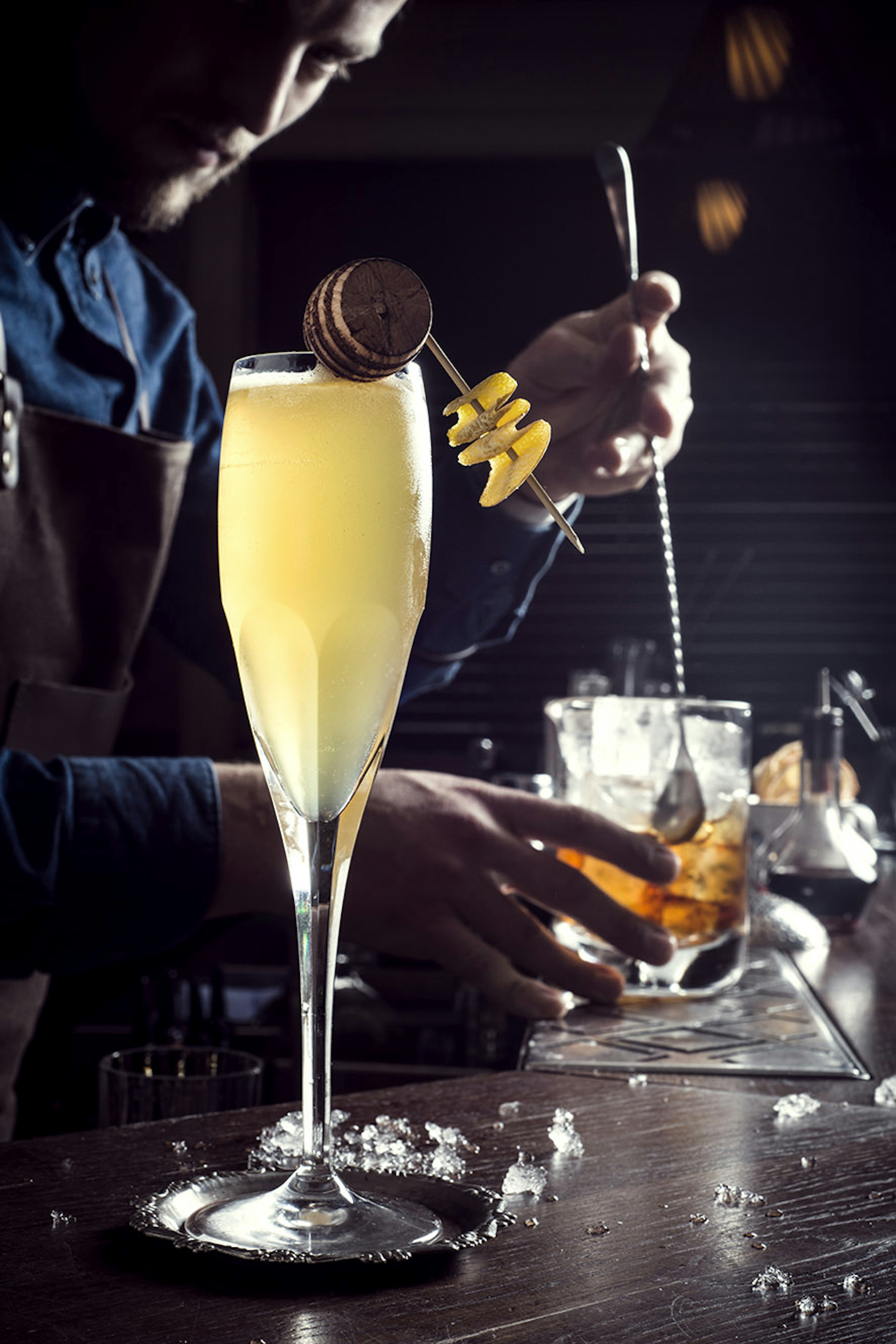 A champagne cocktail sits on the bar with a man in the background mixing a whisky drink at Imperial Craft Cocktail Bar, Tel Aviv © Imperial Craft Cocktail Bar