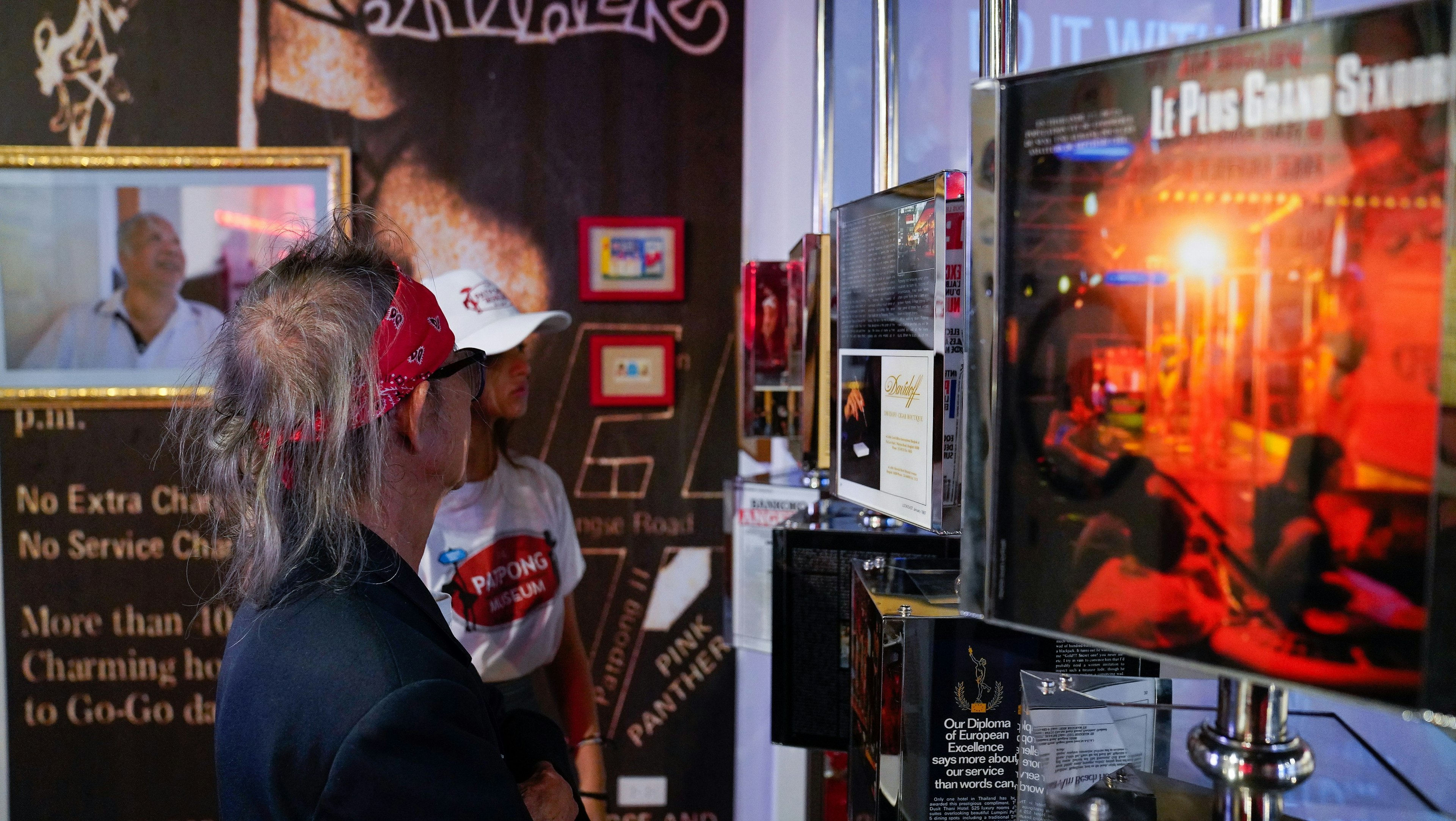 A man and woman peruse various images of the history of Bangkok's Patpong district inside the Patpong Museum. The walls are adorned with images of the district from throughout the last fifty years.