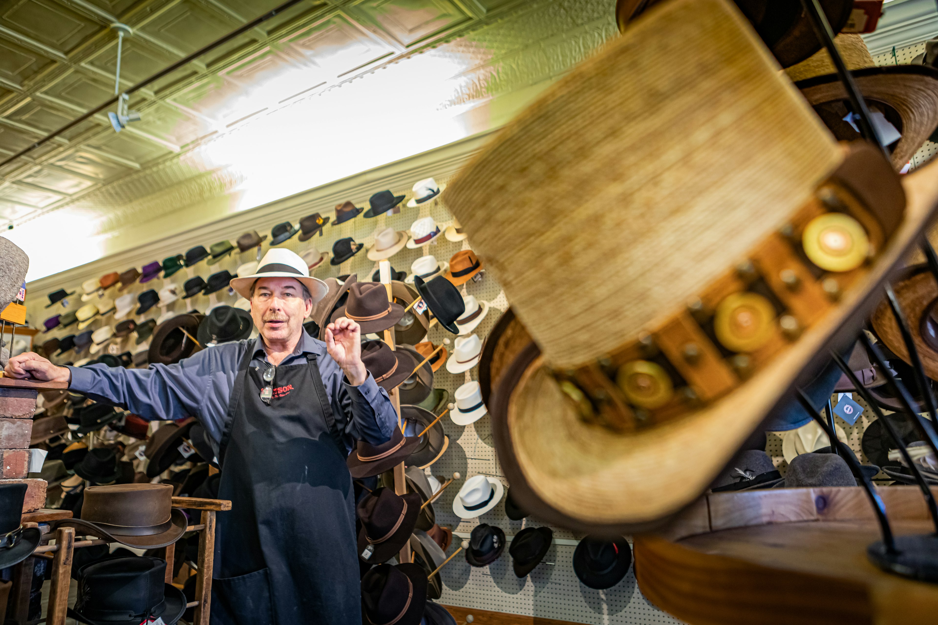 Jack Kellogg stands in the background surrounded by top hats, some decorated with steampunk accessories