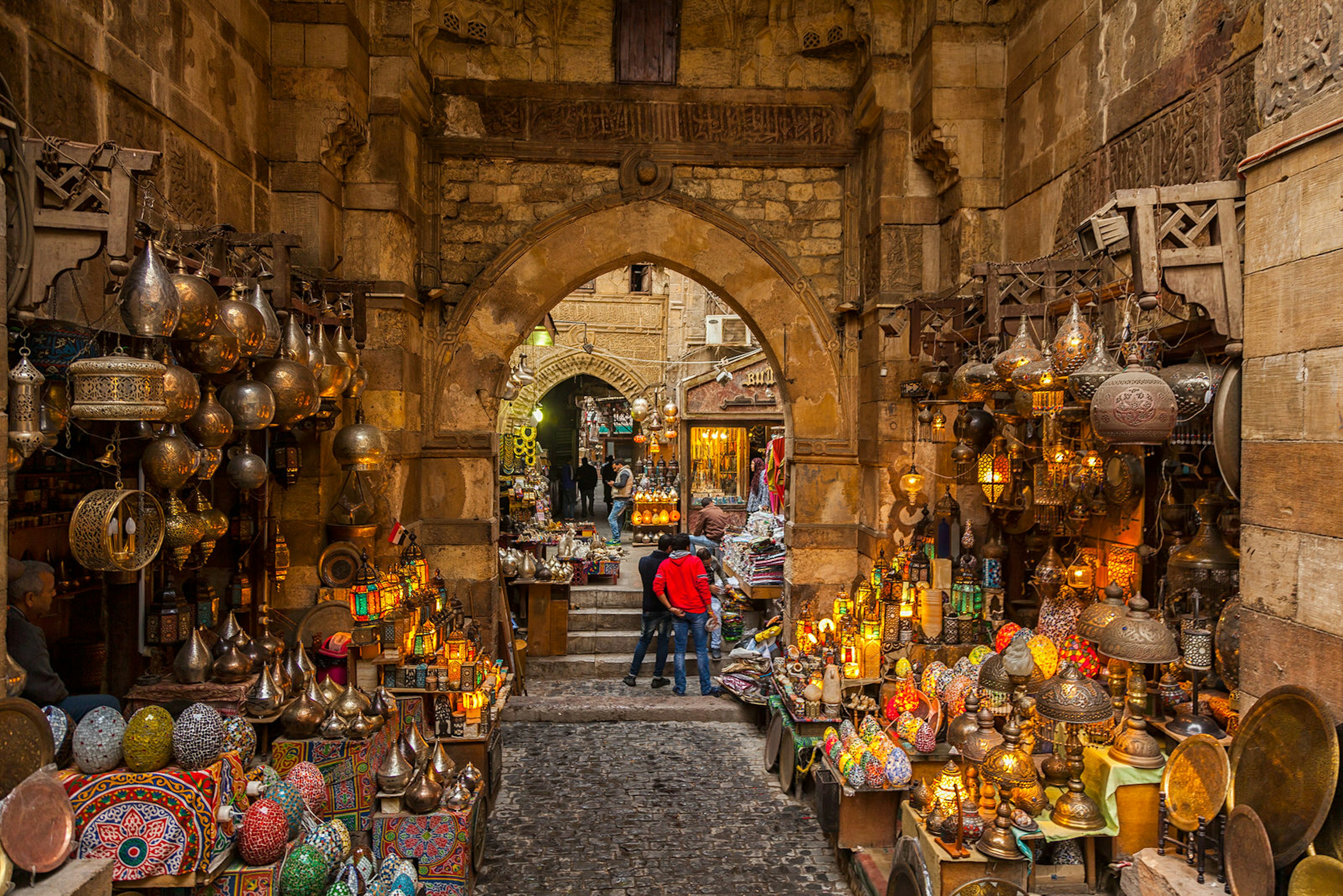 Lamps line the walls on either side of the path through the narrow market alleyway