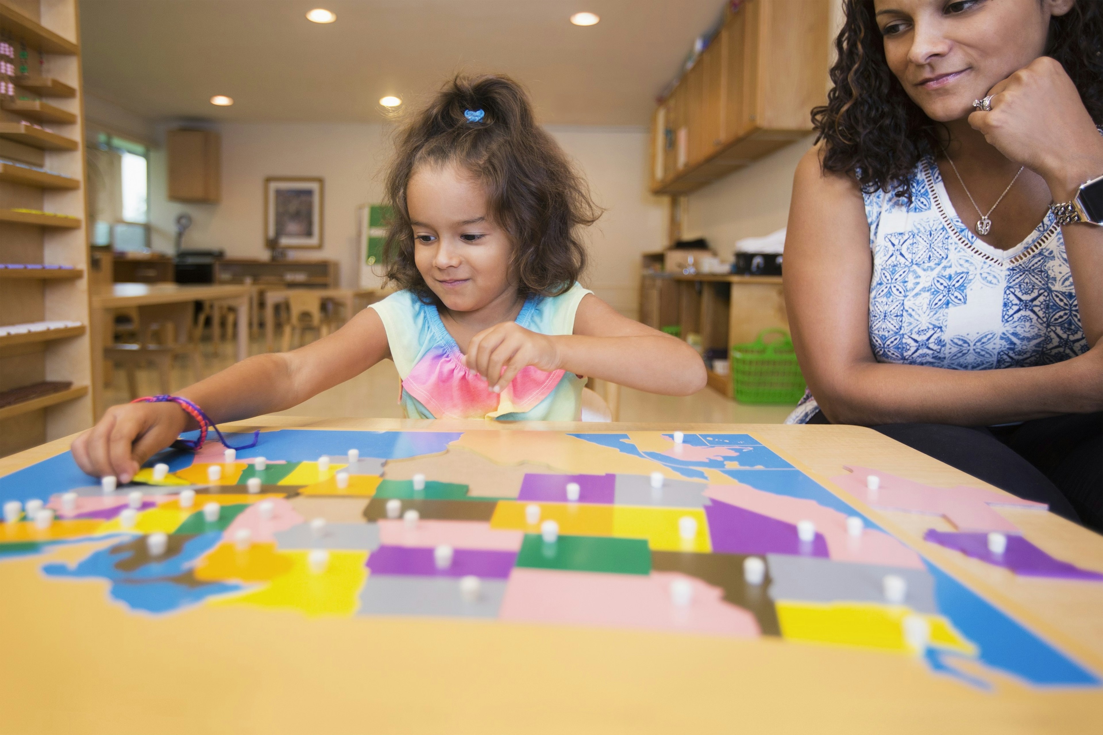 A young girl places the final pieces in a colourful jigsaw of the USA, while an adult watches on