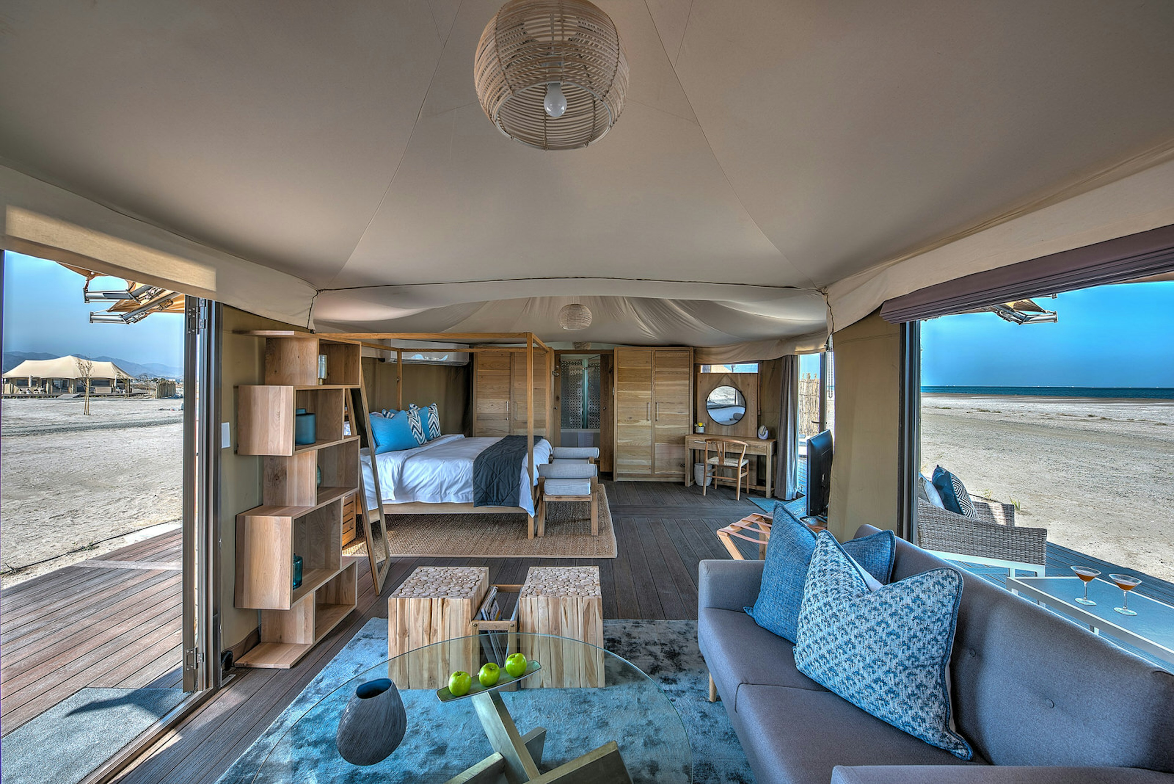 Blue and pine interiors of the Kingfisher Lodge glamping tent, including a couch, glass coffee table, double bed and bookshelves.