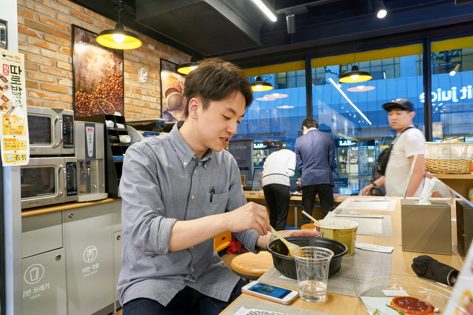 A man stirs a bowl of instant noodles in a cooking area. Most convenience stores have a cooking area where you can make elaborate ramen, microwaved meals, coffee and drinks © Sorbis / Shutterstock