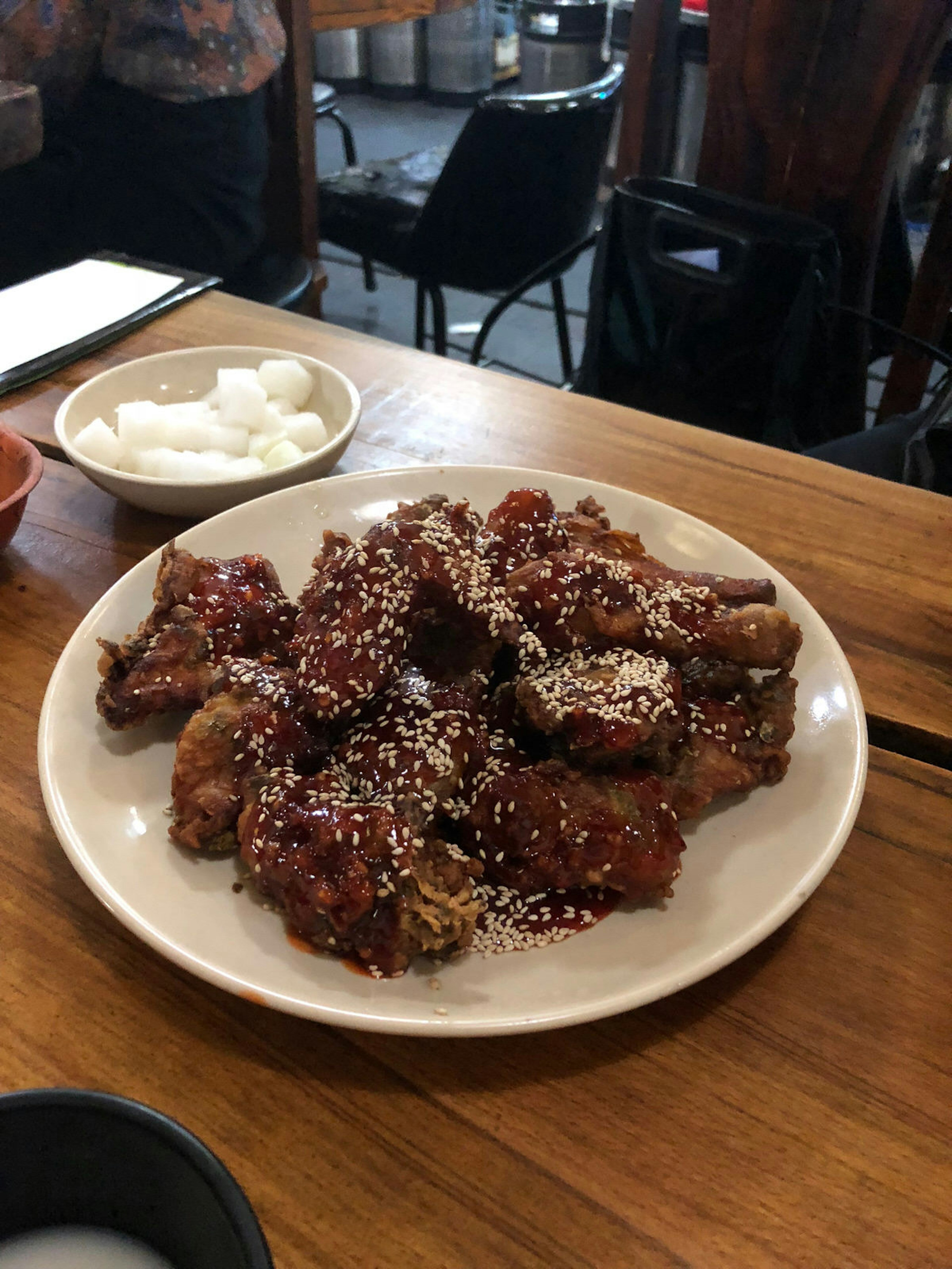 A plate of marinated Korean fried chicken covered in sesame seeds on a wooden table