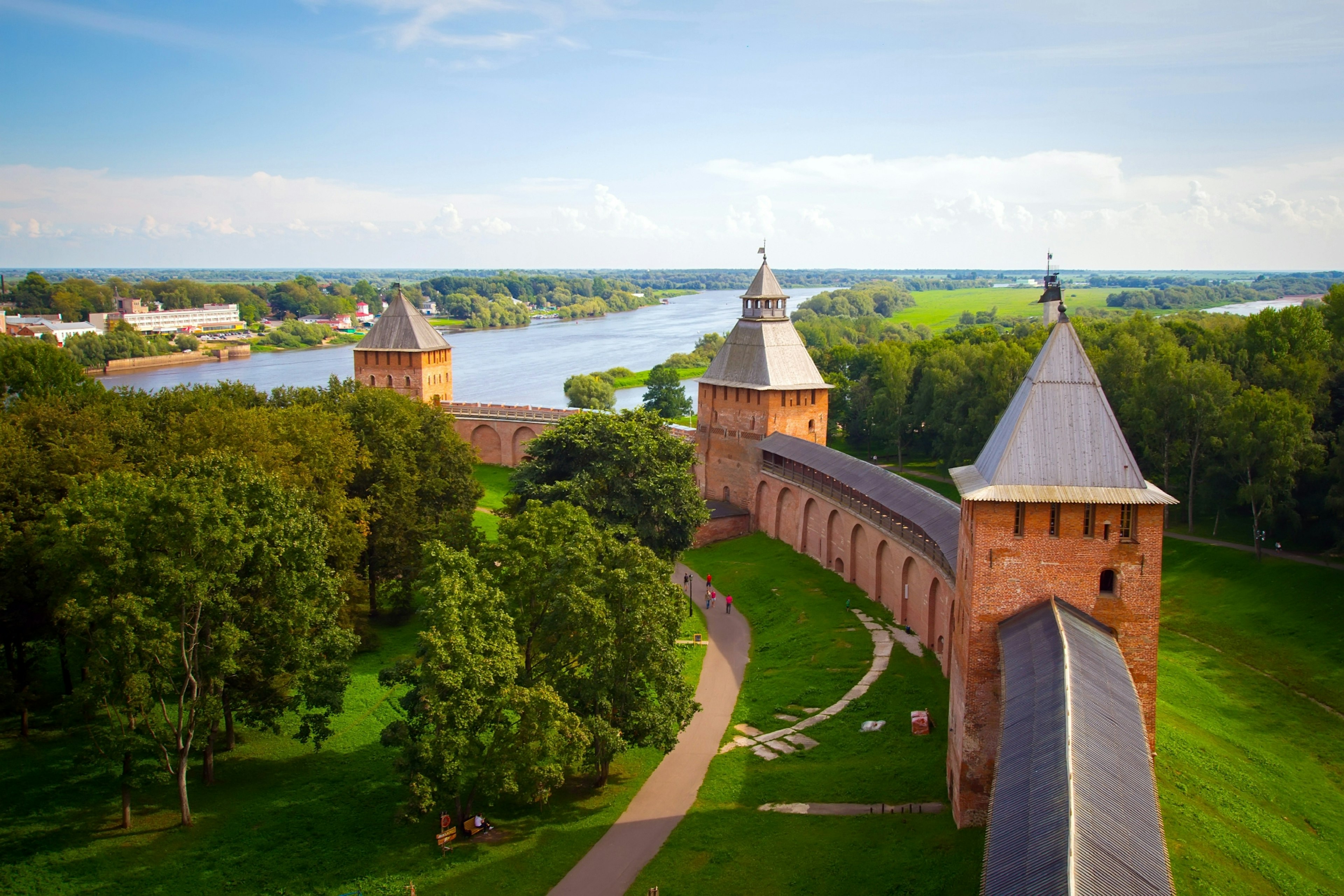 Substantial brick battlements with three towers running through grassland and down to a river