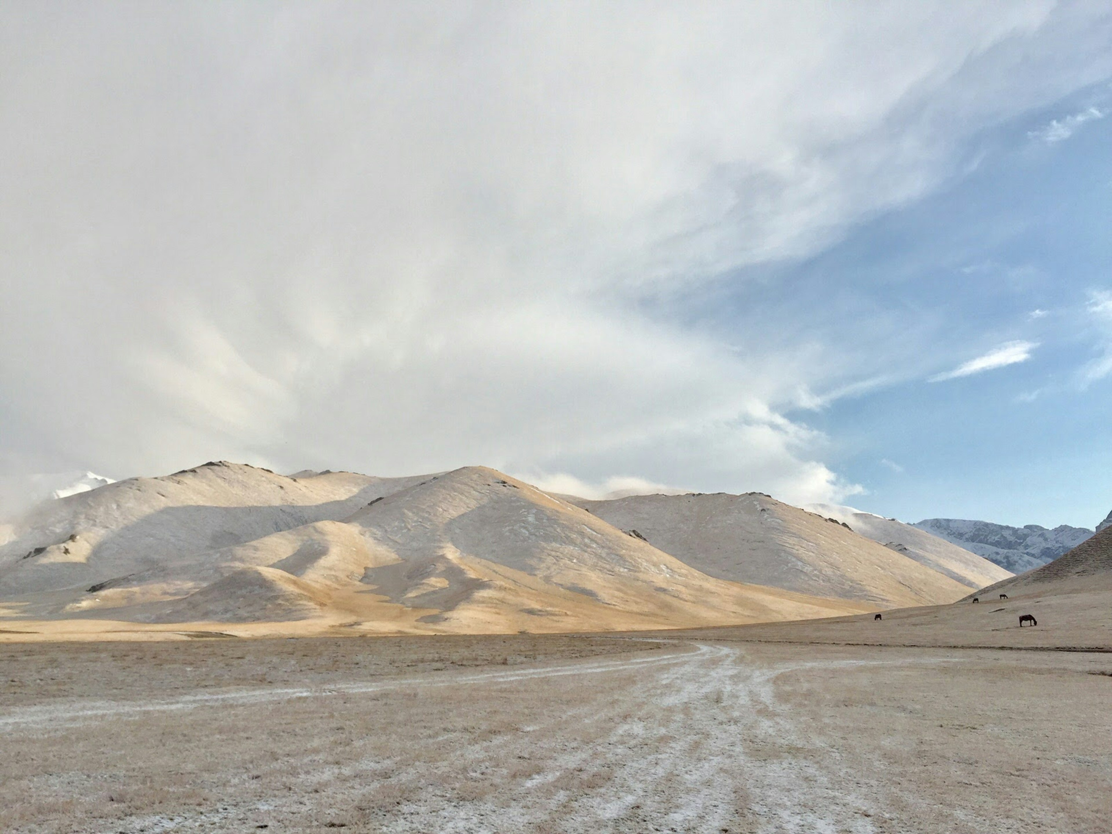 Tan and brown mountains in the distance with a light dusting of white snow, and white clouds above © Megan Eaves / Lonely Planet